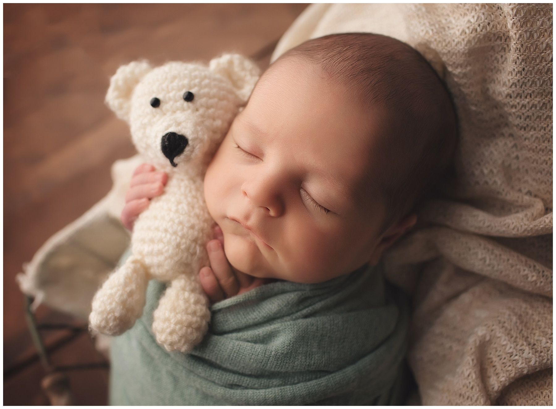 A newborn baby is wrapped in a blanket and holding a teddy bear.