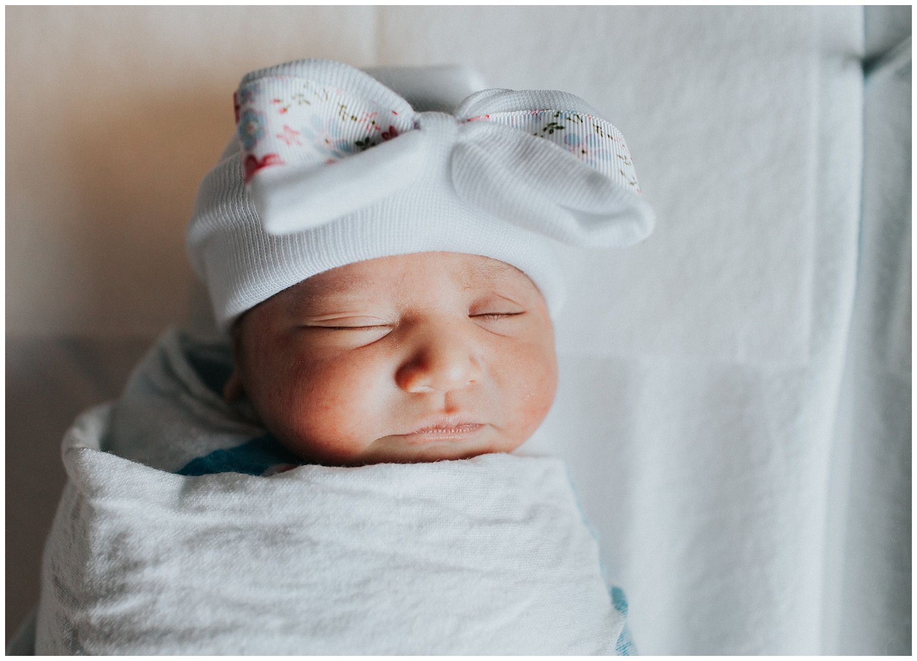 A newborn baby is wrapped in a blanket and wearing a white hat.