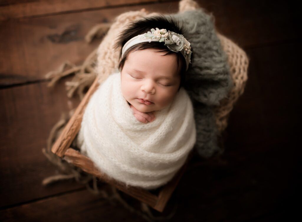 A newborn baby wrapped in a white blanket is sleeping in a basket.
