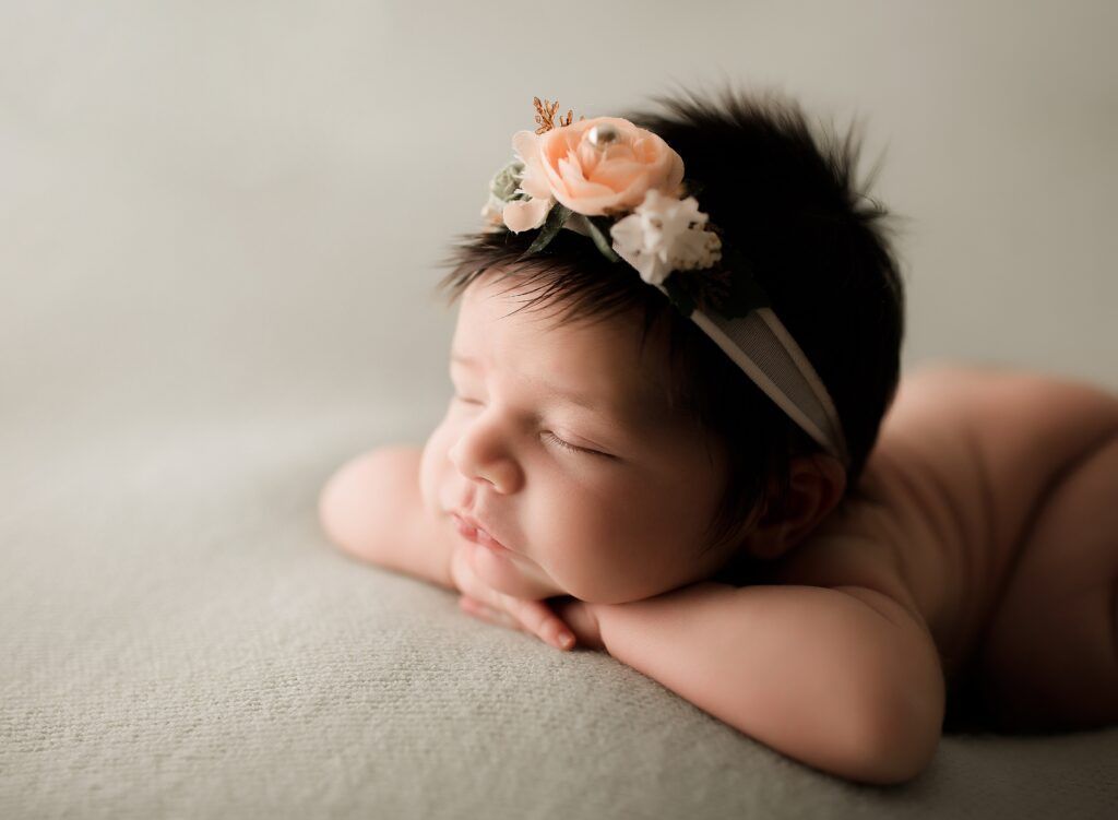 A newborn baby girl wearing a flower headband is sleeping on a blanket.
