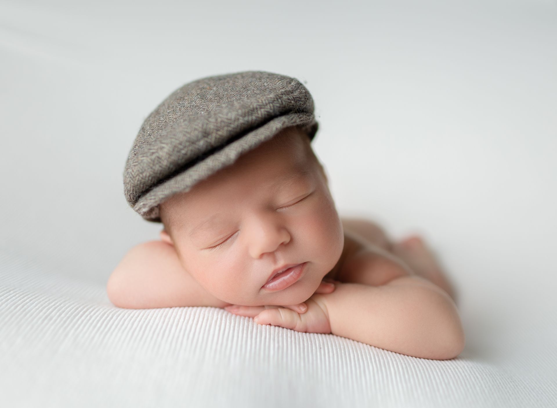 A newborn baby wearing a hat is sleeping on a white blanket.