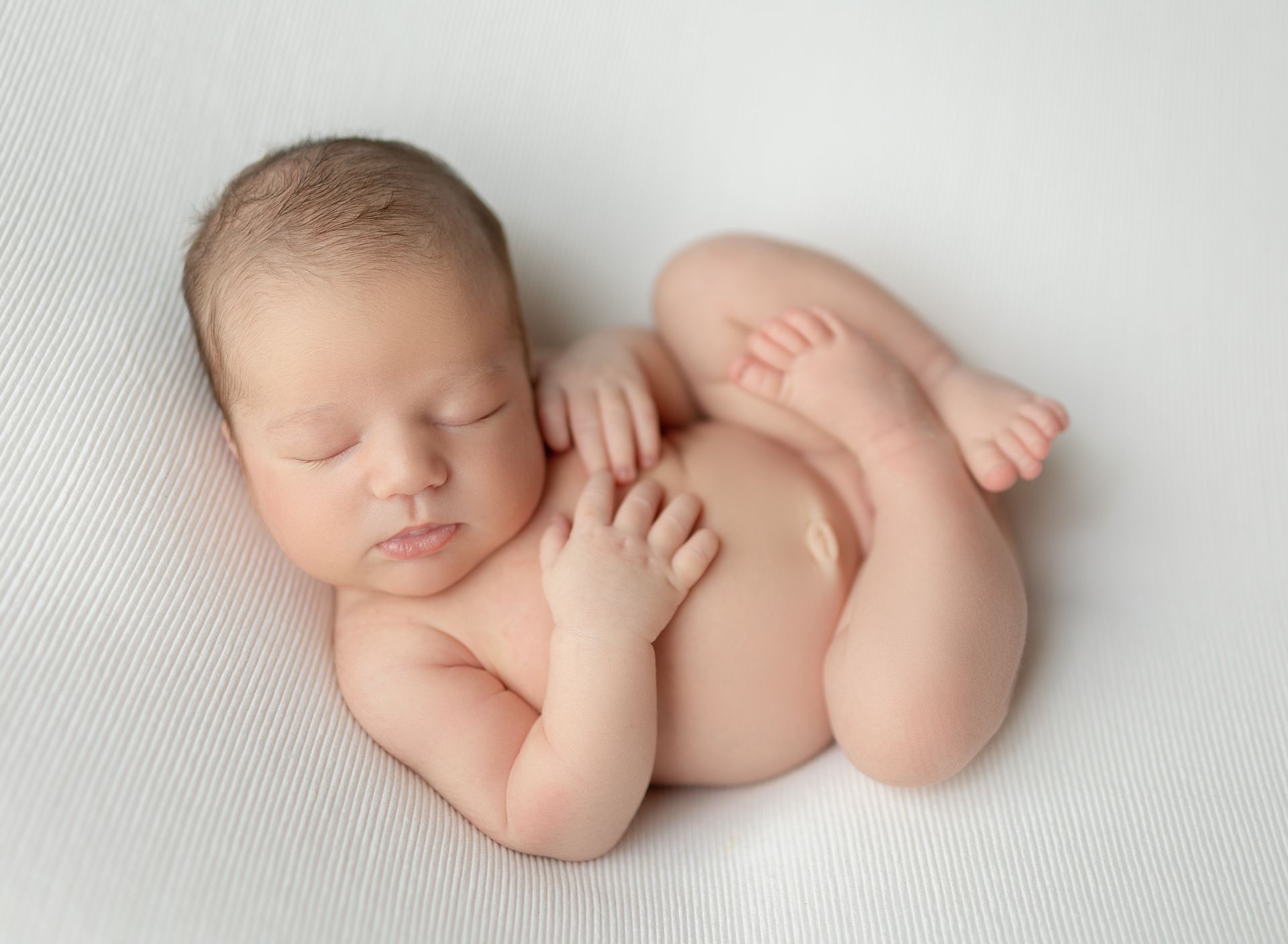 A newborn baby is sleeping on a white blanket.