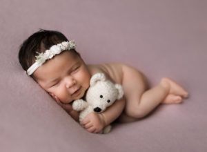 A newborn baby is laying on a pink blanket holding a teddy bear.