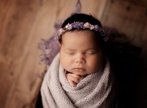 A newborn baby is wrapped in a blanket and wearing a flower crown.