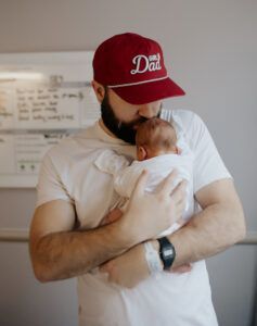 A man wearing a red hat is holding a baby in his arms.