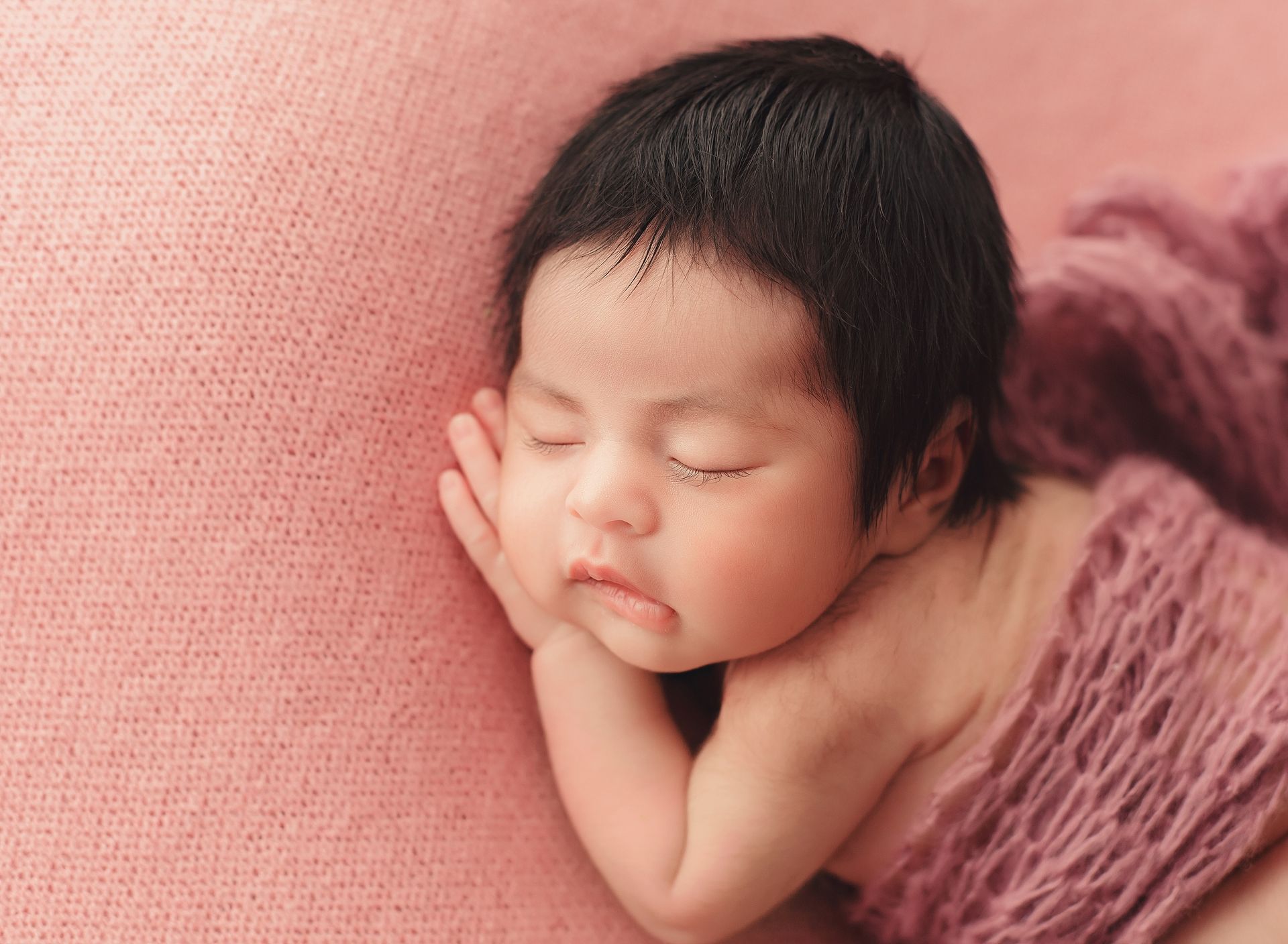 A newborn baby wrapped in a pink blanket is sleeping on a pink blanket.