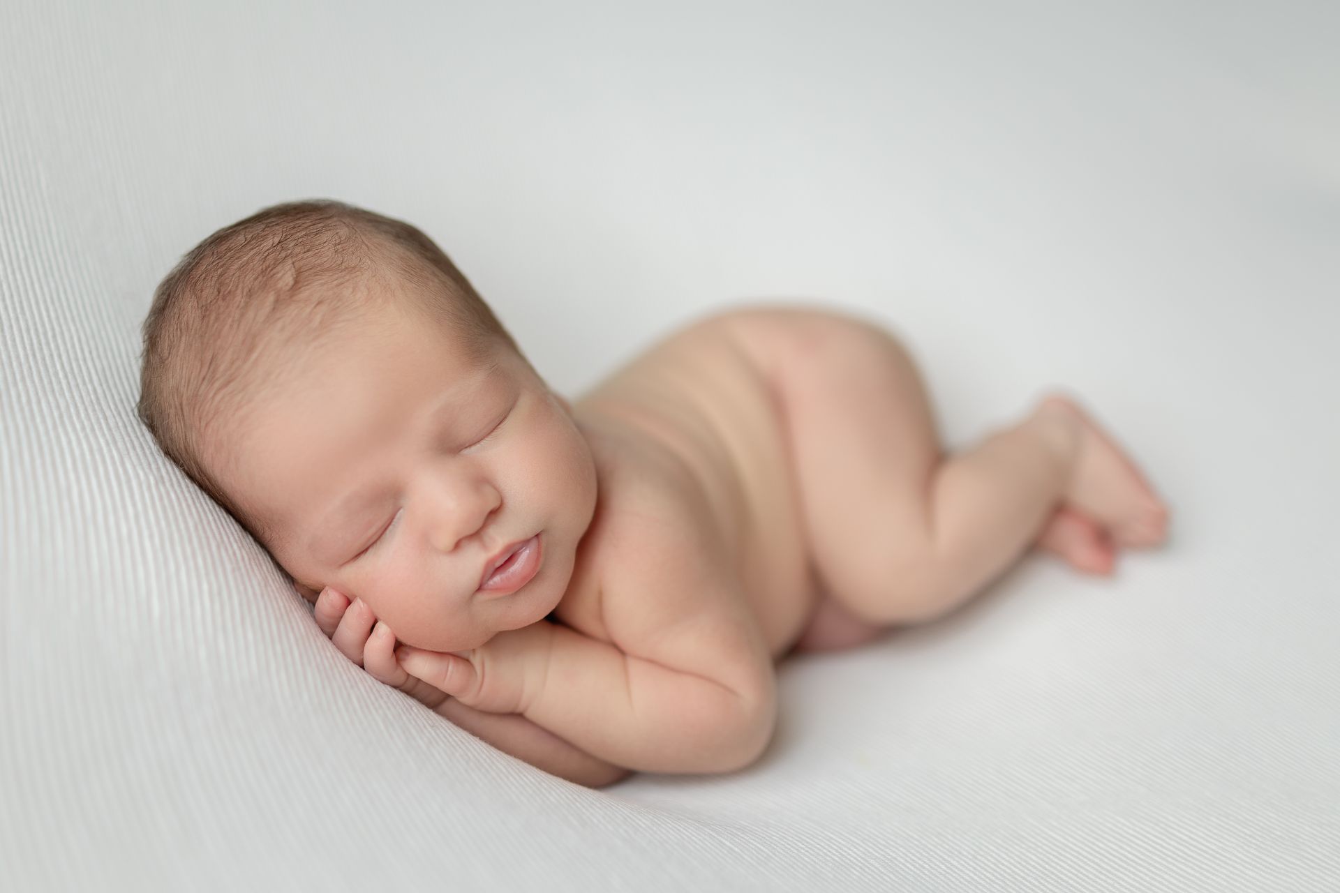 A newborn baby is sleeping on it's side  on a white blanket.