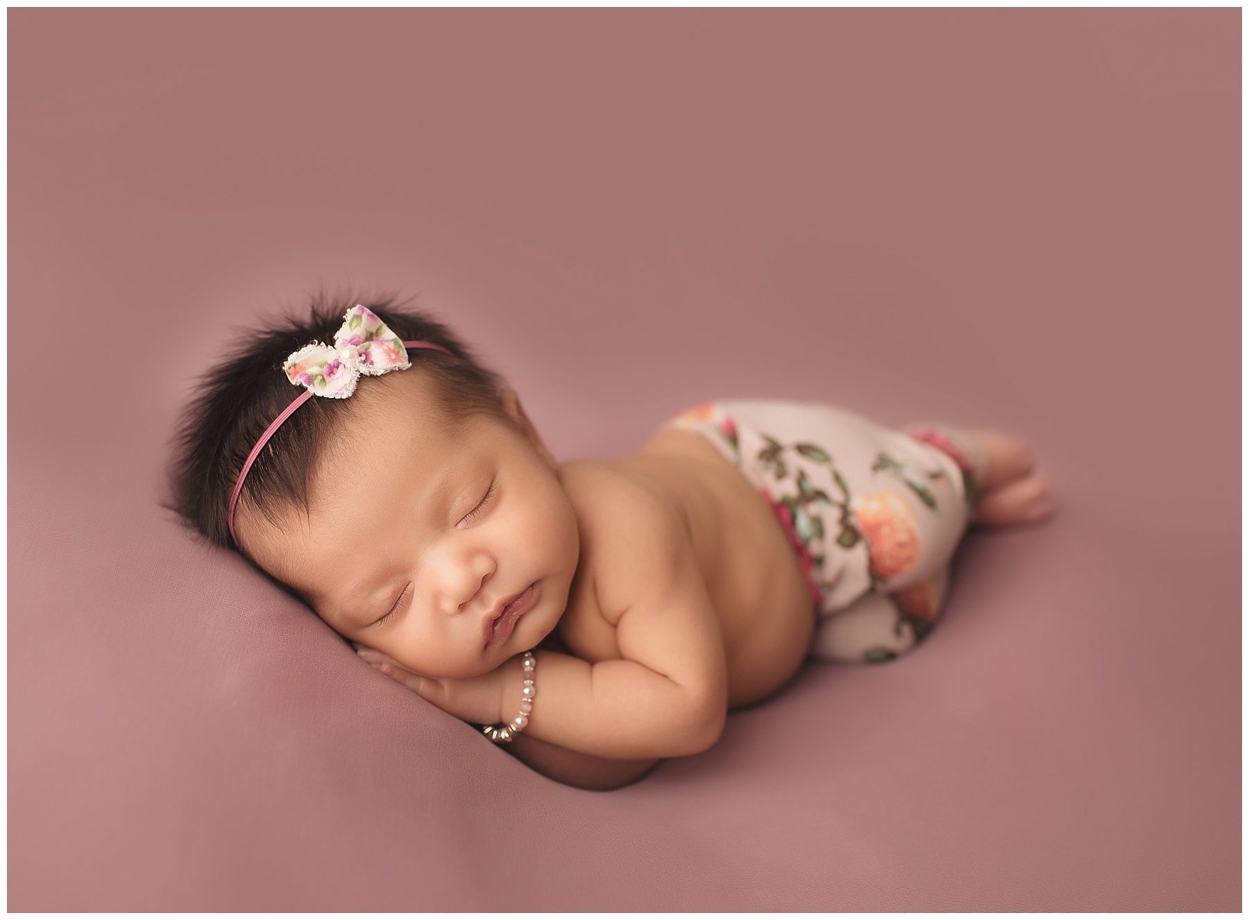 A newborn baby girl is sleeping on a pink blanket.