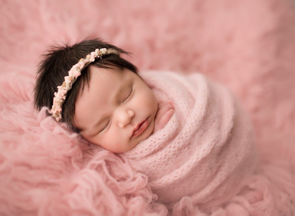 A newborn baby wrapped in a pink blanket is sleeping on a pink blanket.