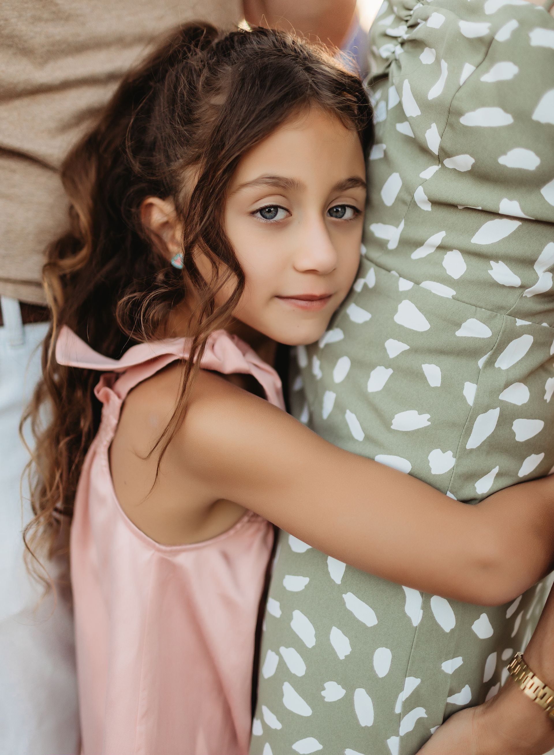 Girl with long brown hair hugs a person in a green dress, looking at the camera.