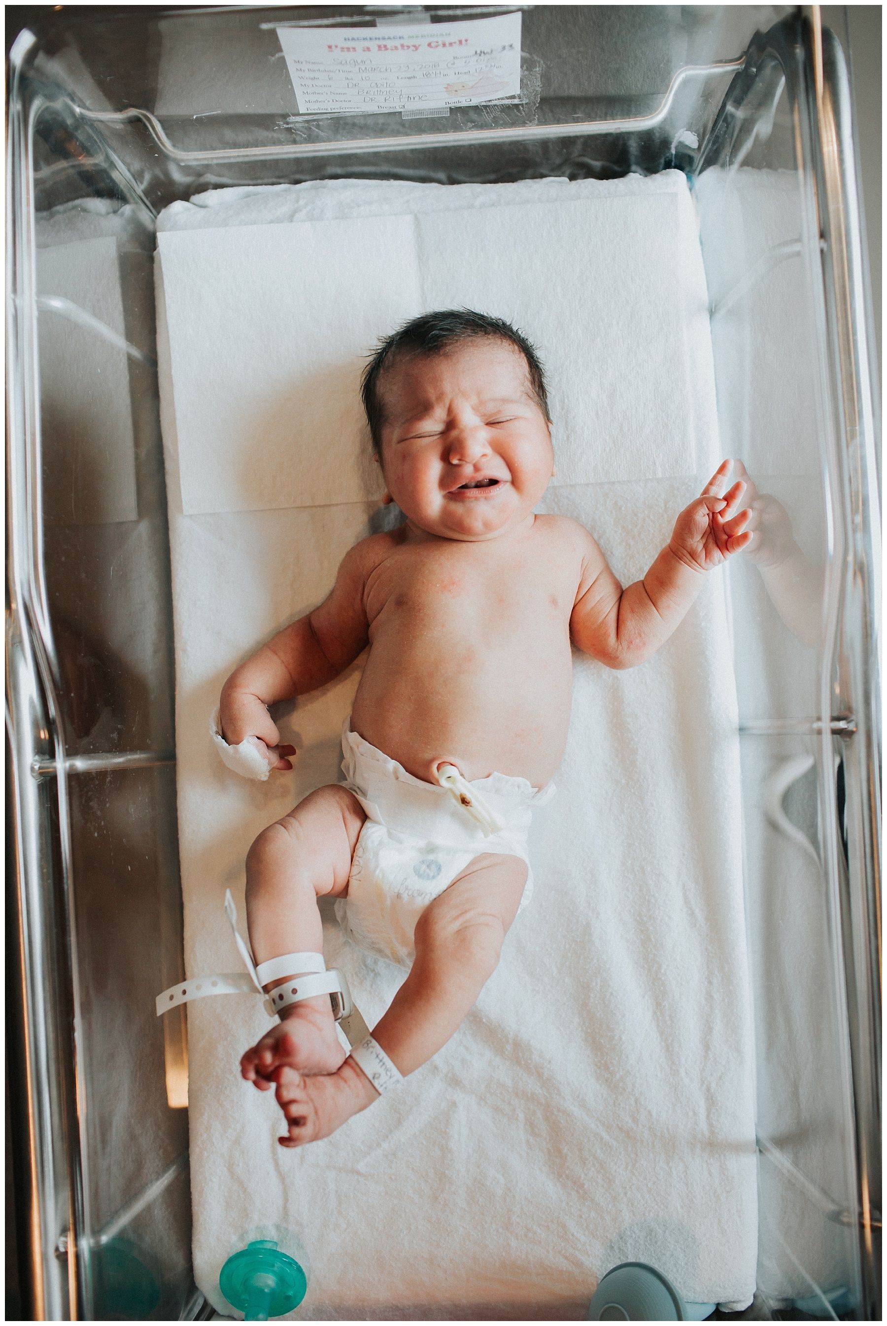 A newborn baby is crying in a hospital bed.