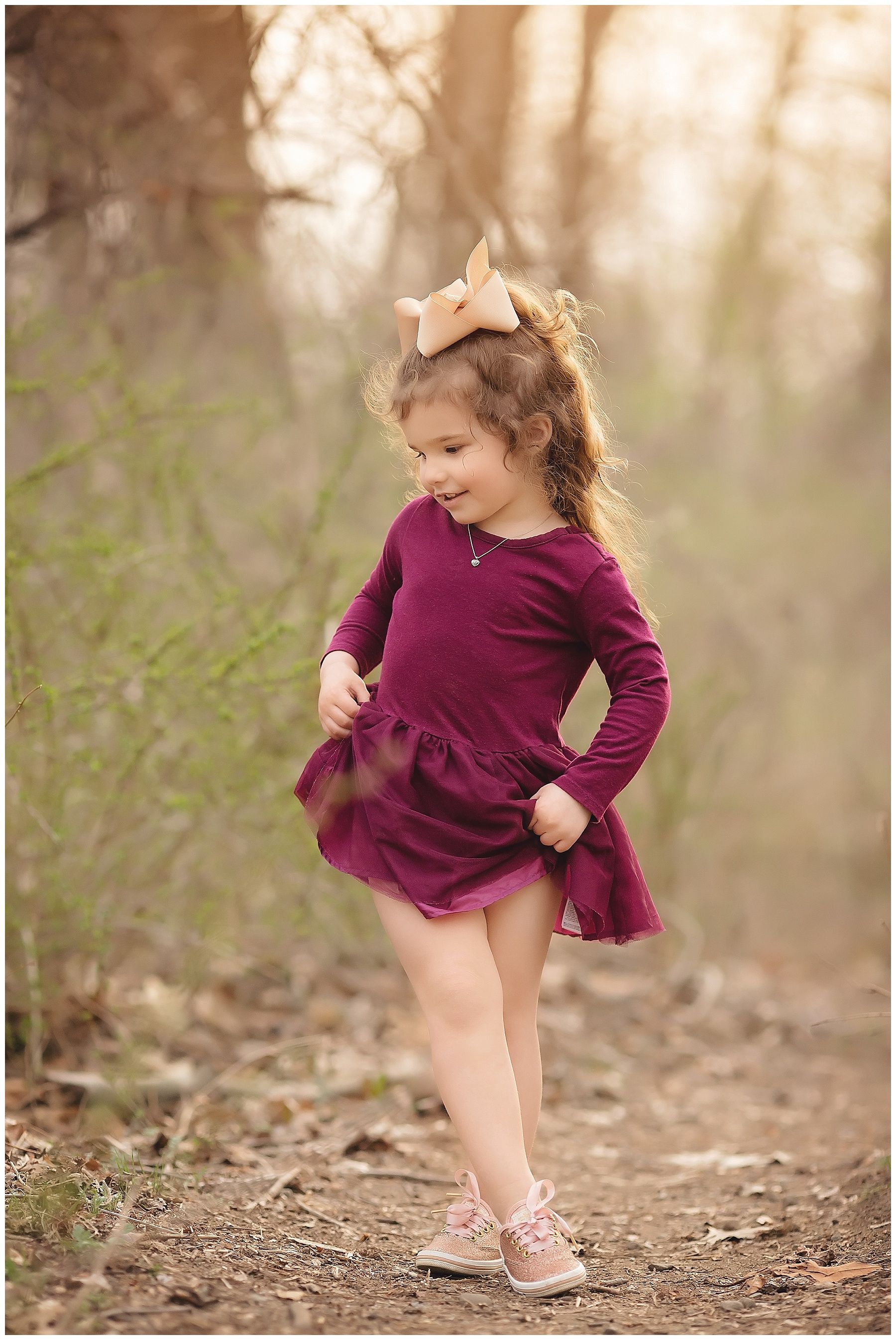 A little girl in a purple dress is standing in the woods.