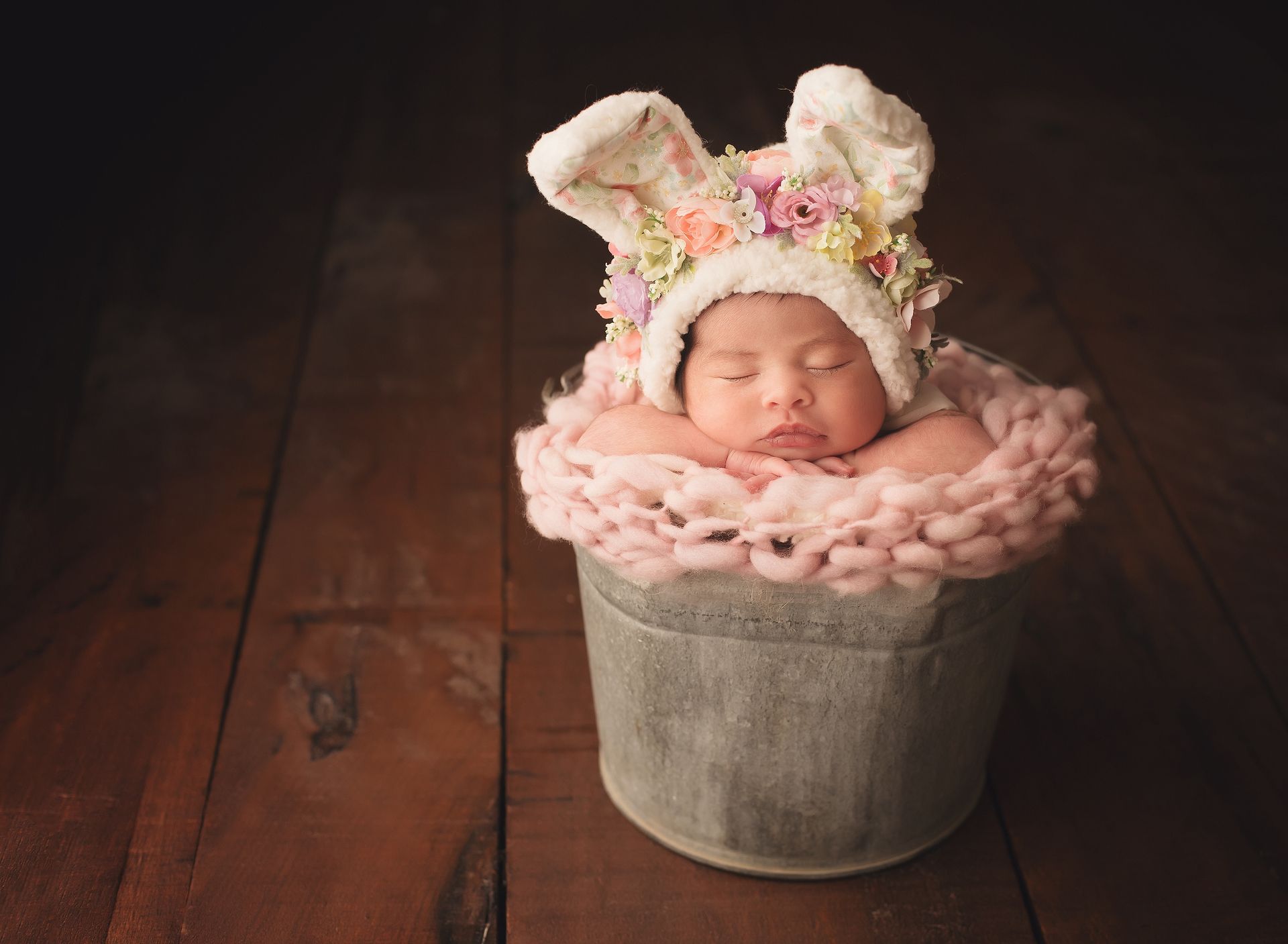 A newborn baby wearing a bunny hat is sleeping in a bucket.