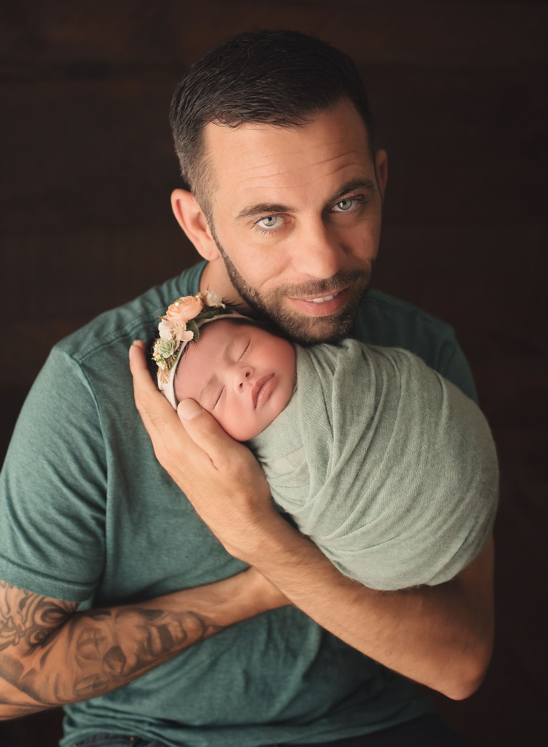 A man is holding a newborn baby wrapped in a green blanket.