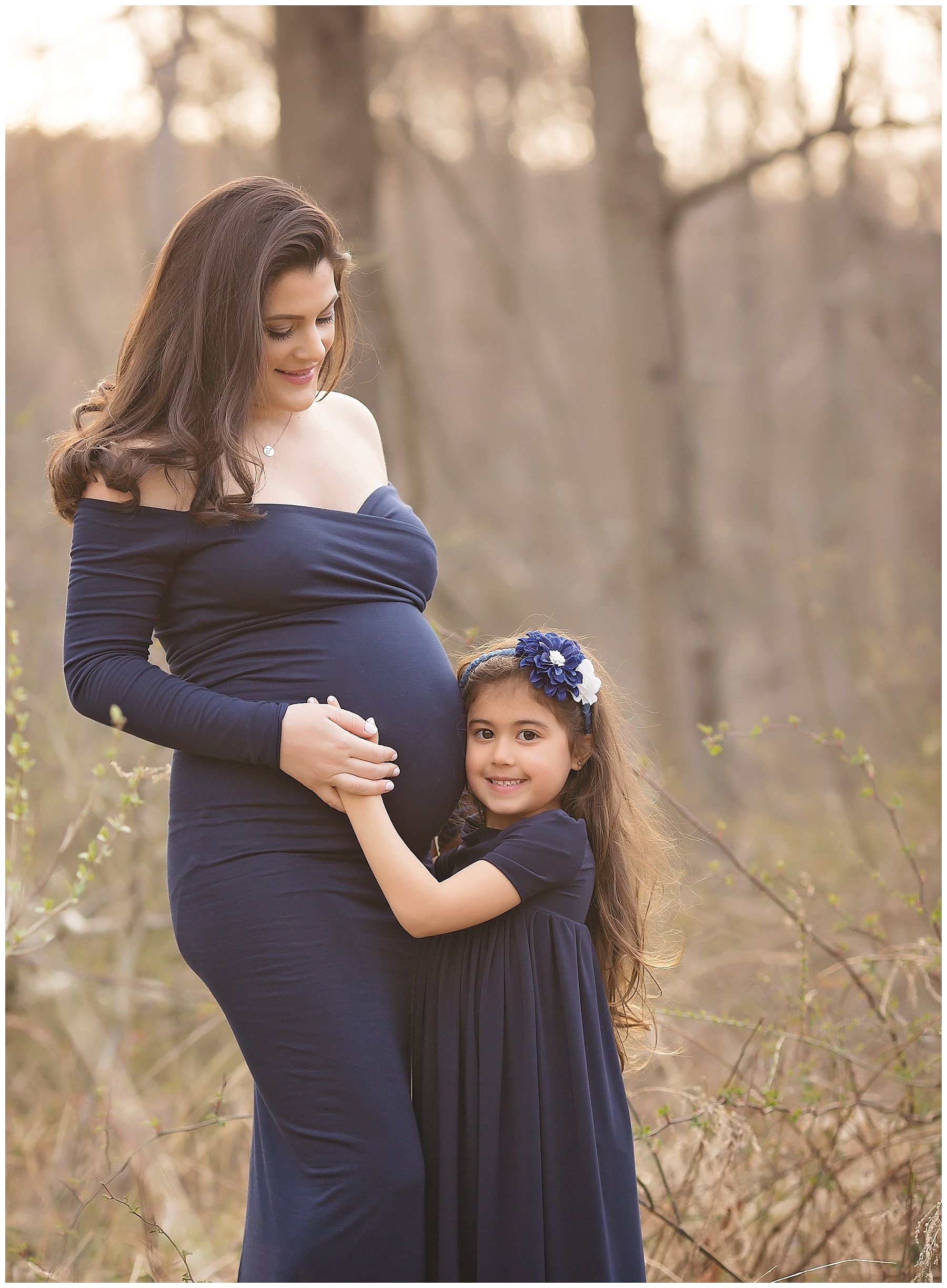 A pregnant woman in a blue dress is standing next to a little girl in a blue dress.