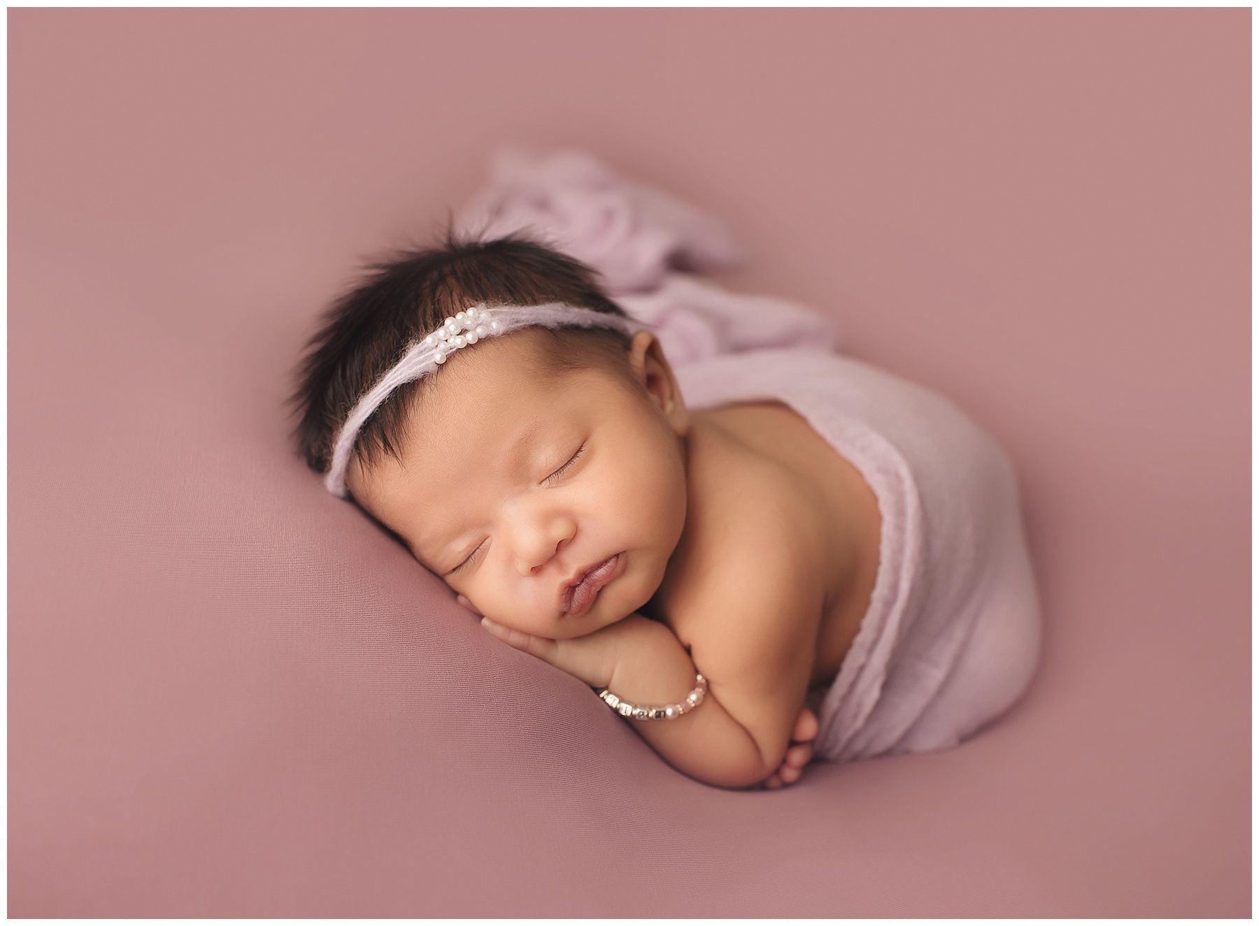 A newborn baby wrapped in a pink blanket is sleeping on a pink blanket.