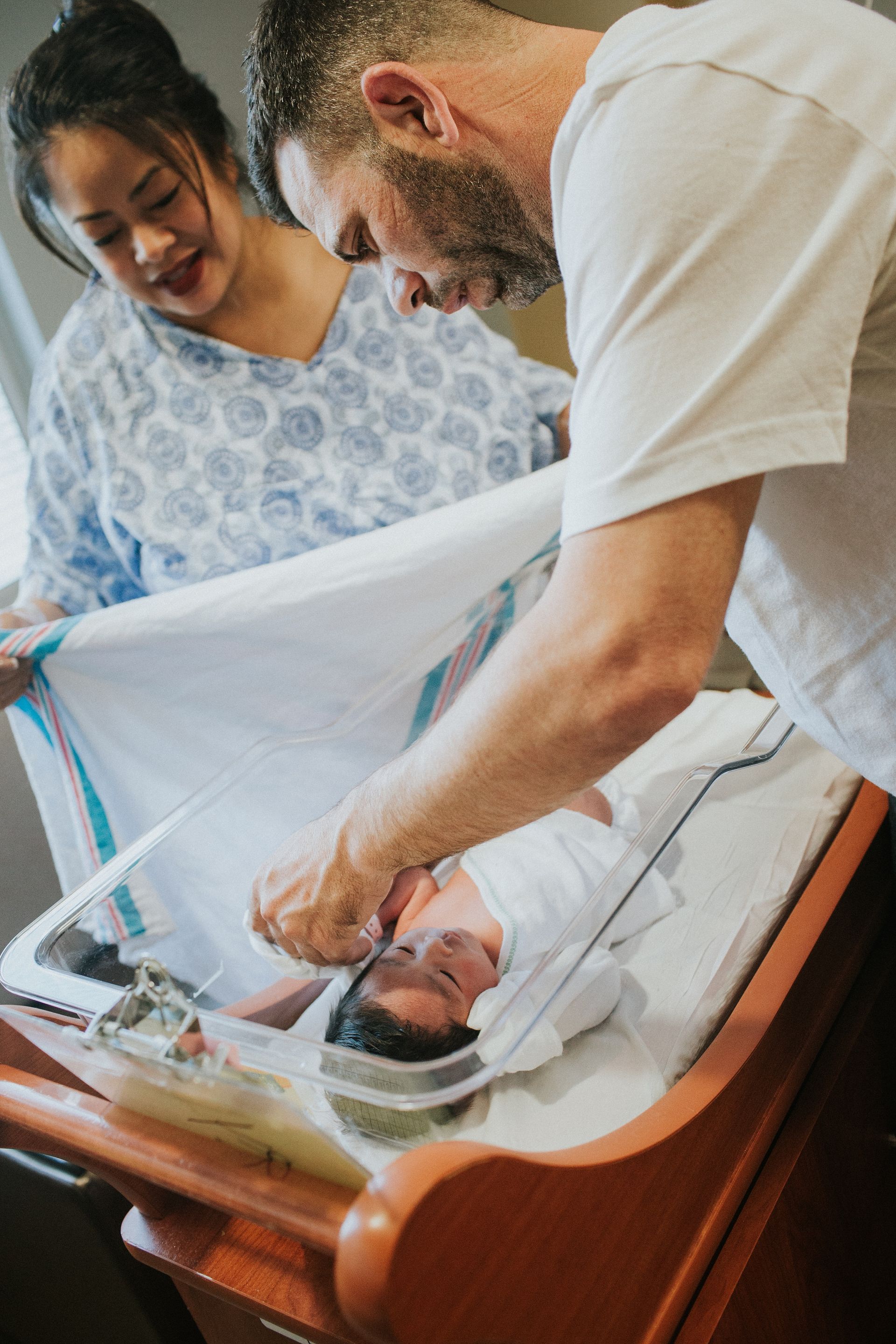 A man and a woman are looking at a newborn baby in a hospital crib.