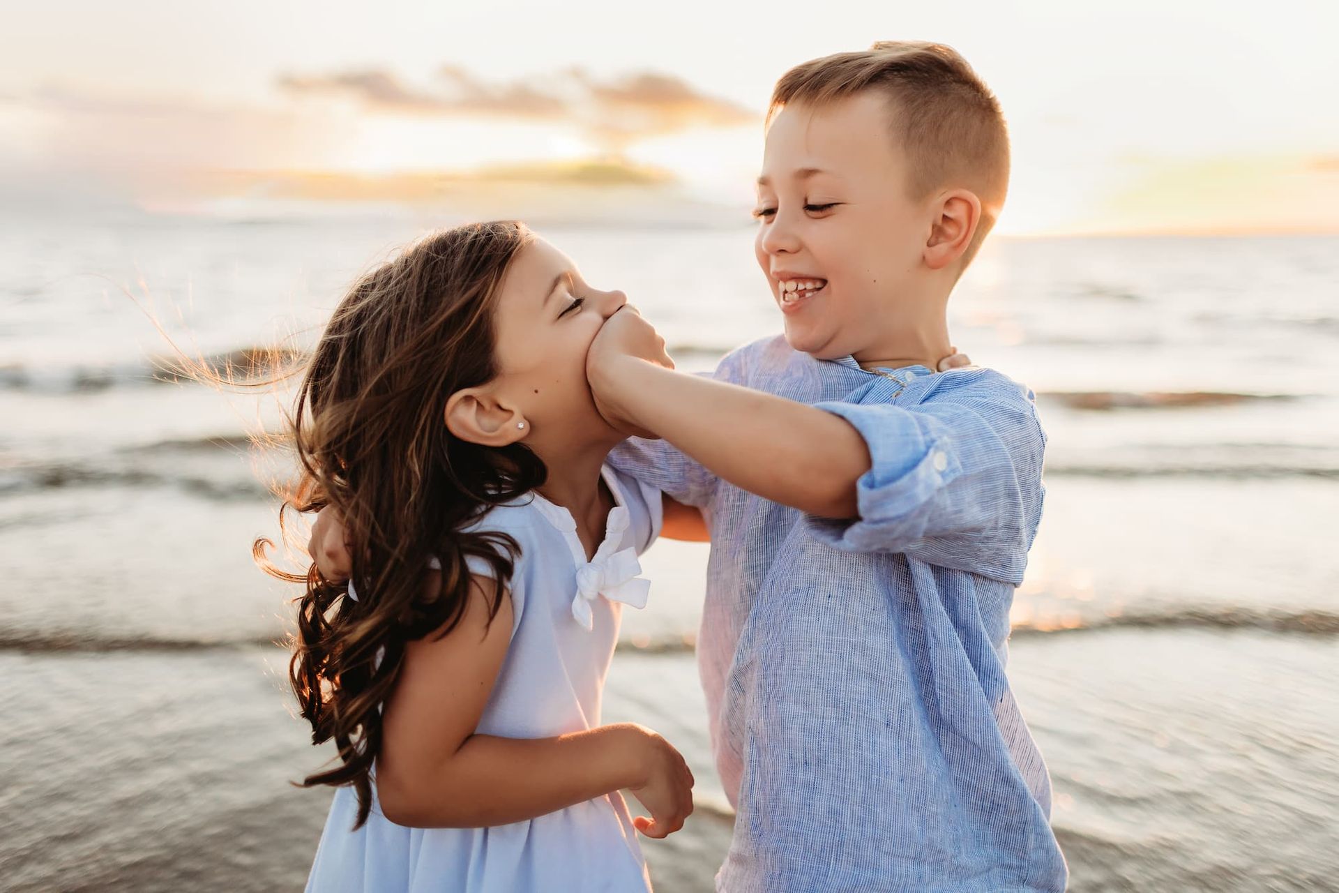 Mother kissing a child, embracing two others on a grassy field at sunset.