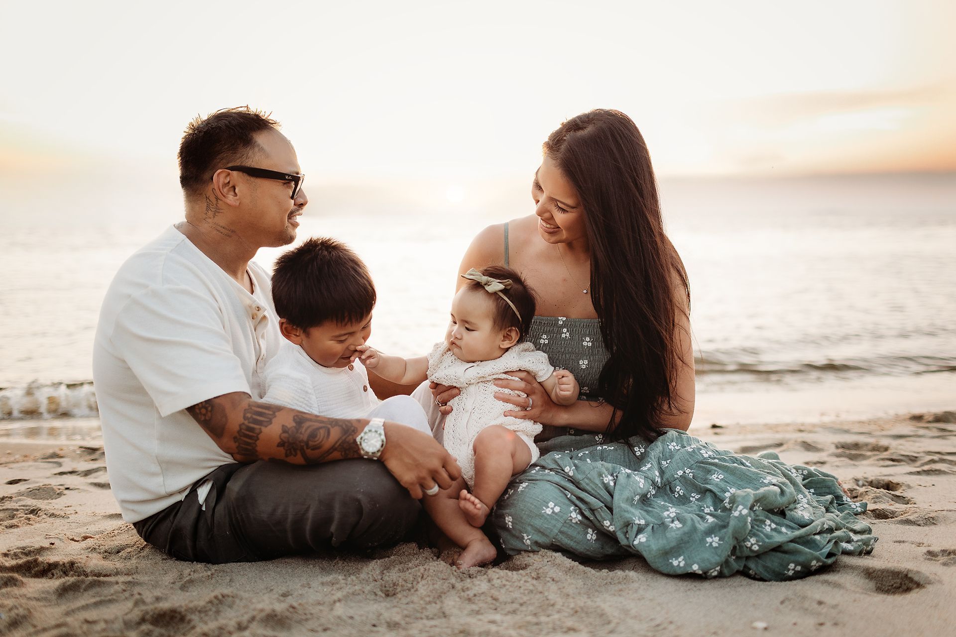 Family of four on beach at sunset: father, mother, and two young children.