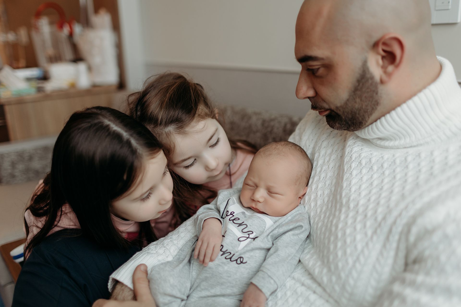A man is holding a newborn baby while two little girls look on.