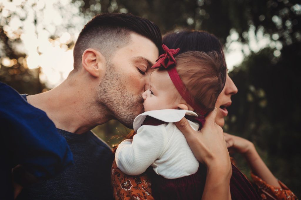 A man and woman are kissing a baby on the cheek.