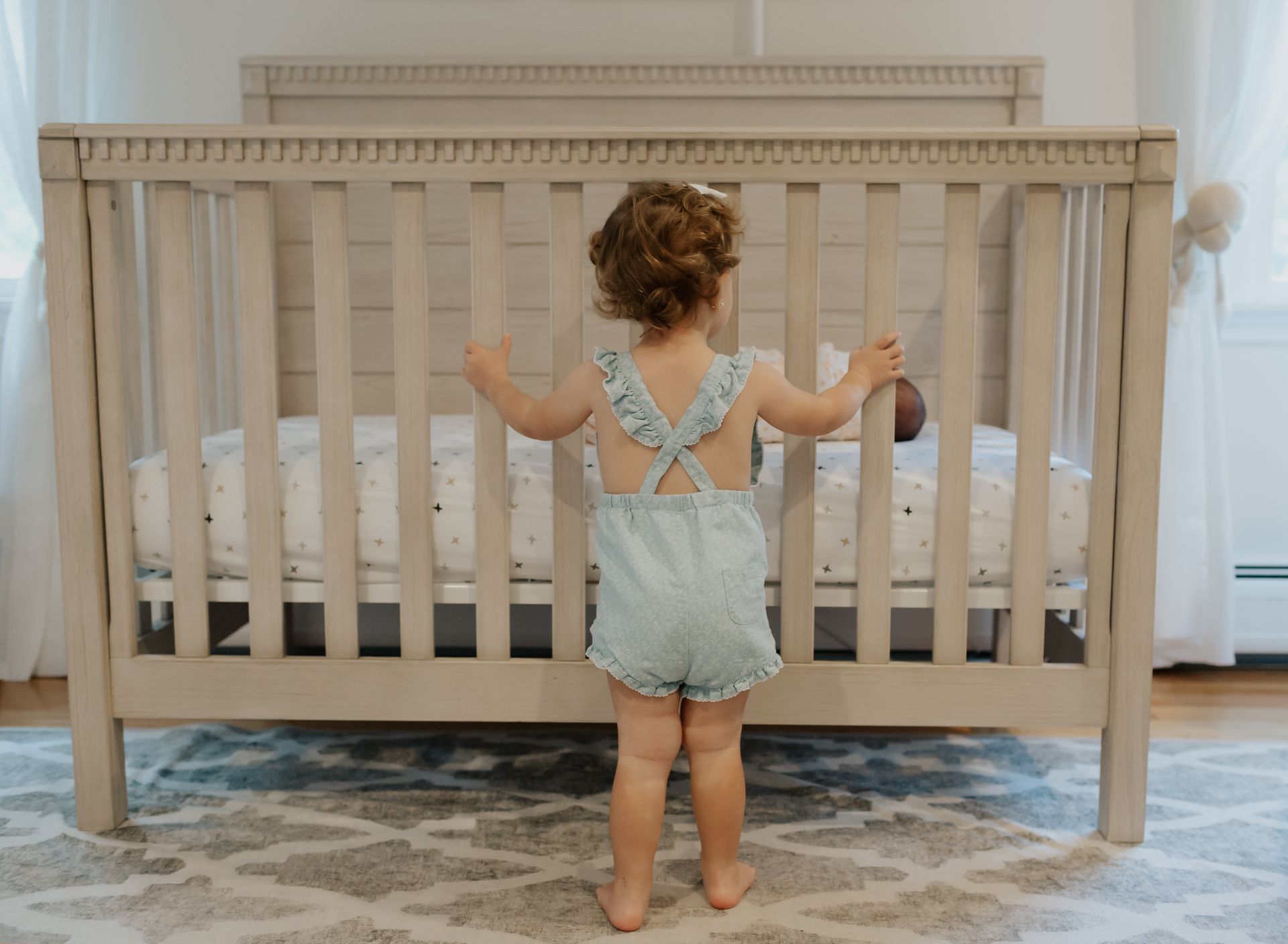 A little girl is standing in front of a crib in a nursery.