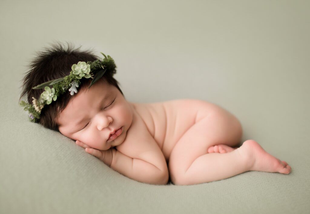 A newborn baby wearing a flower crown is sleeping on a blanket.