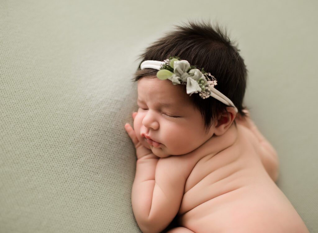 A newborn baby girl wearing a flower headband is sleeping on a blanket.