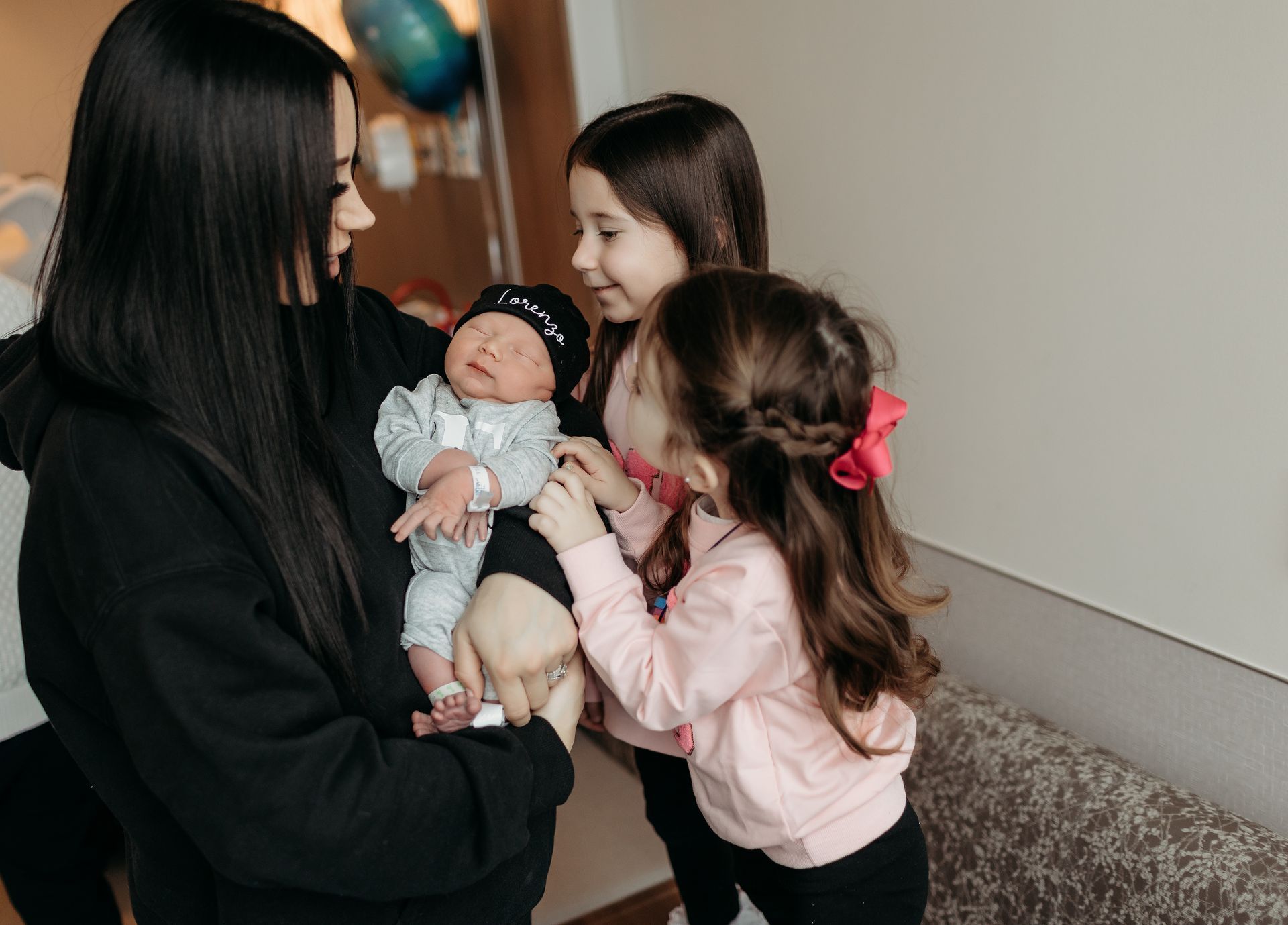 A woman is holding a newborn baby while two little girls look on.