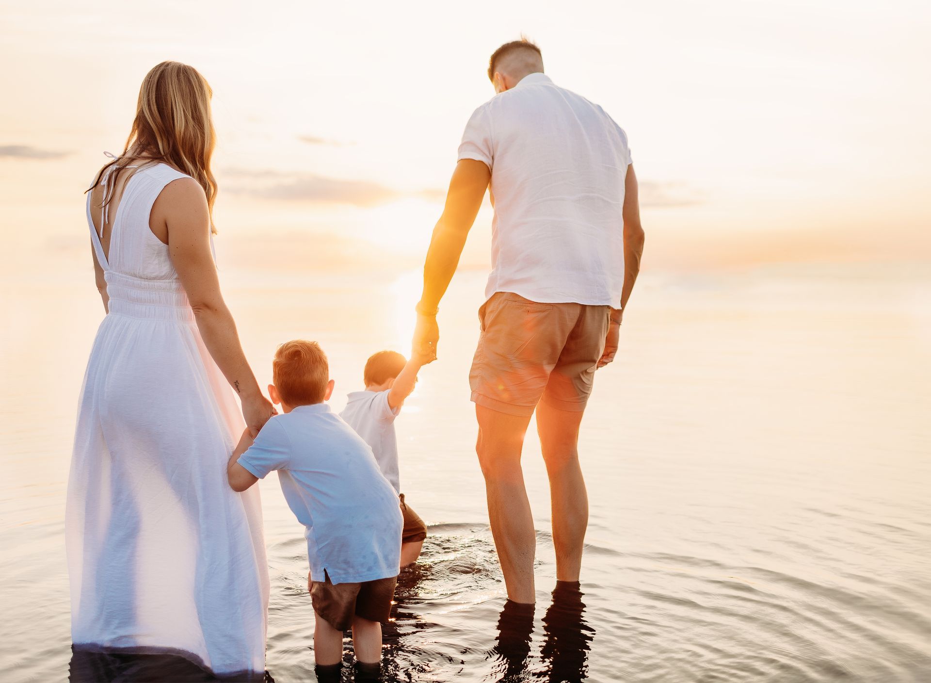 Family wading in water at sunset, holding hands.