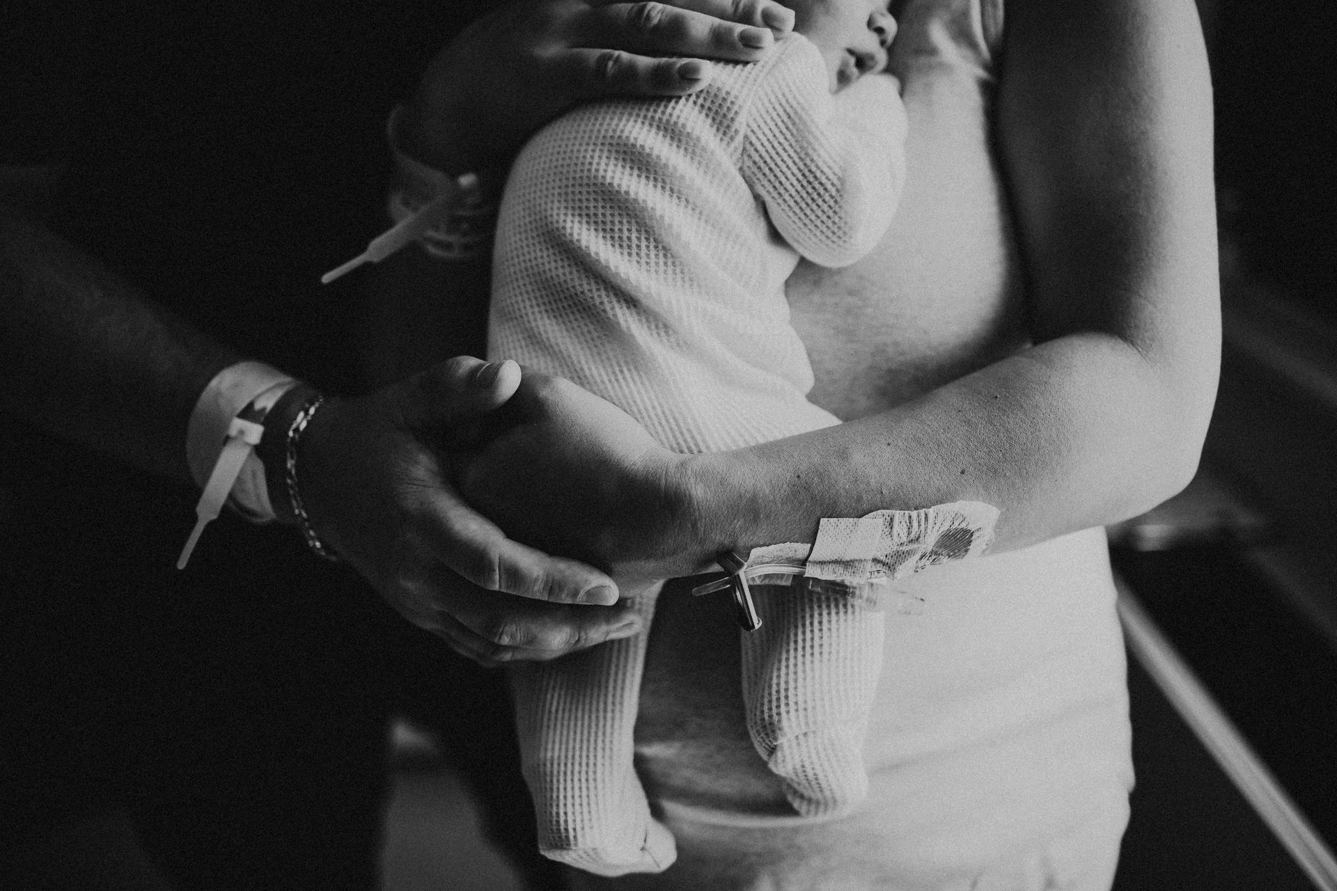 Person holding swaddled newborn, both with hospital wristbands.