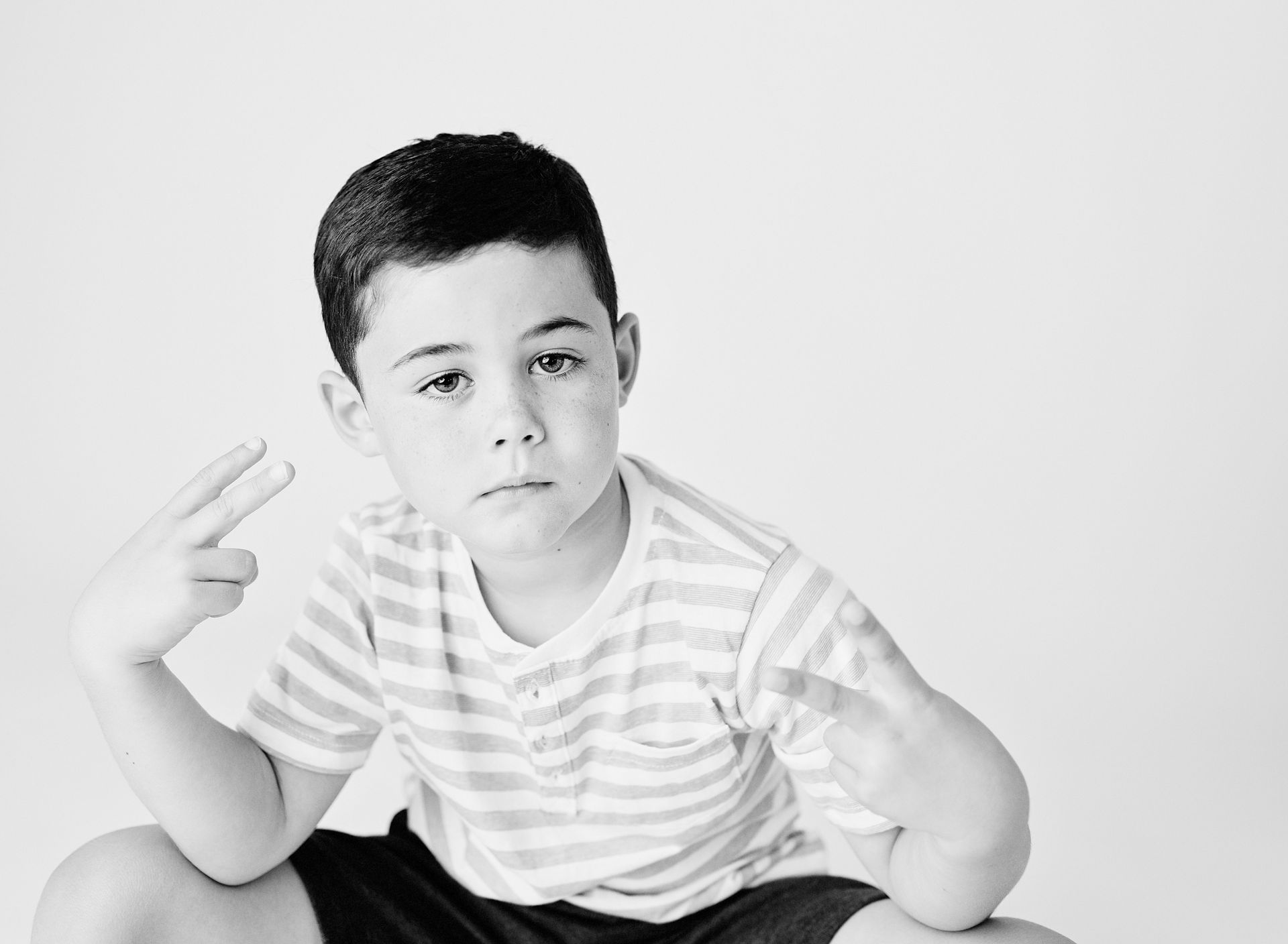 Boy in striped shirt makes a peace sign with one hand, looking at the camera.