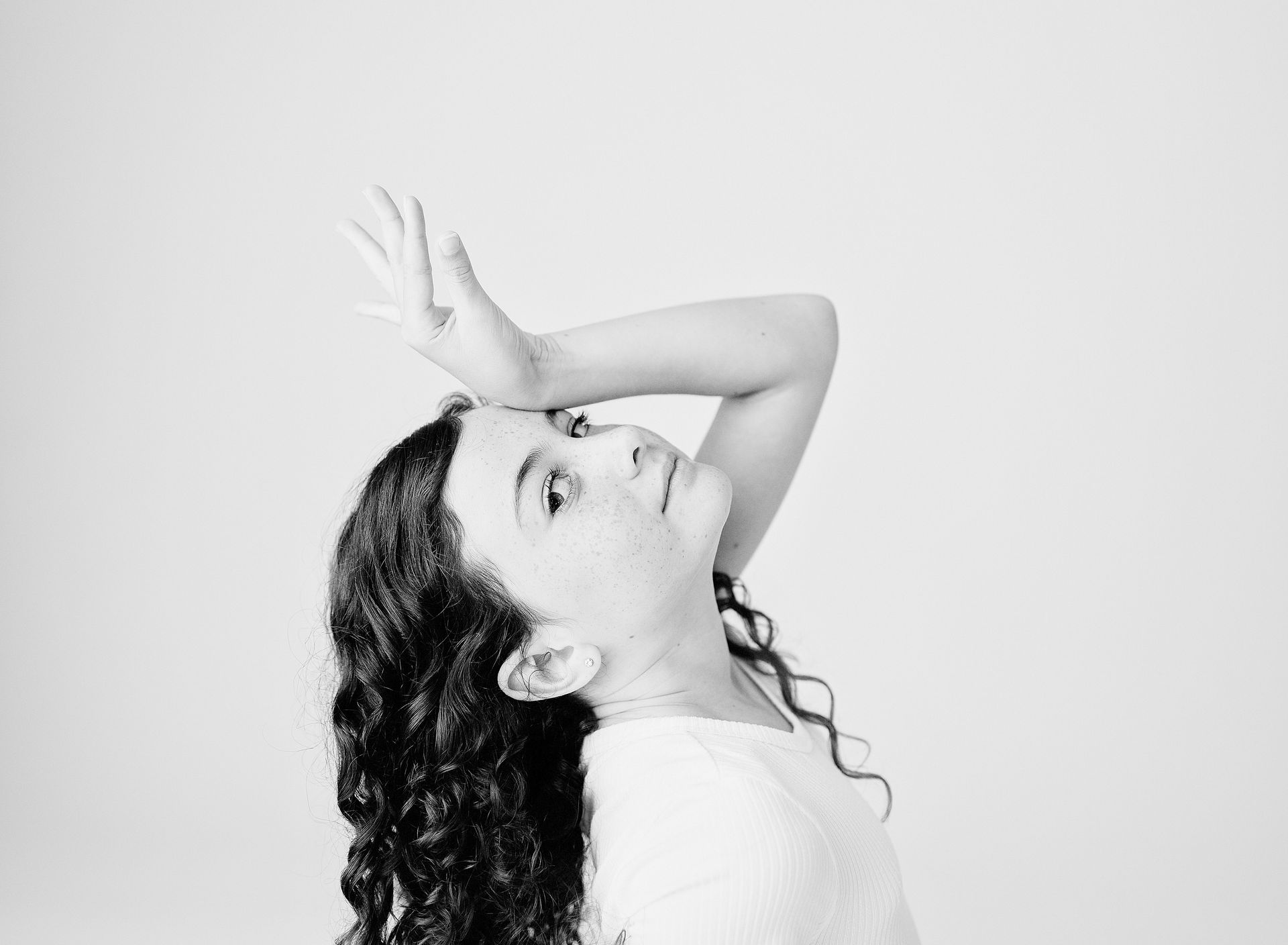 Girl with curly hair, hand to forehead, looking upwards with a thoughtful expression.