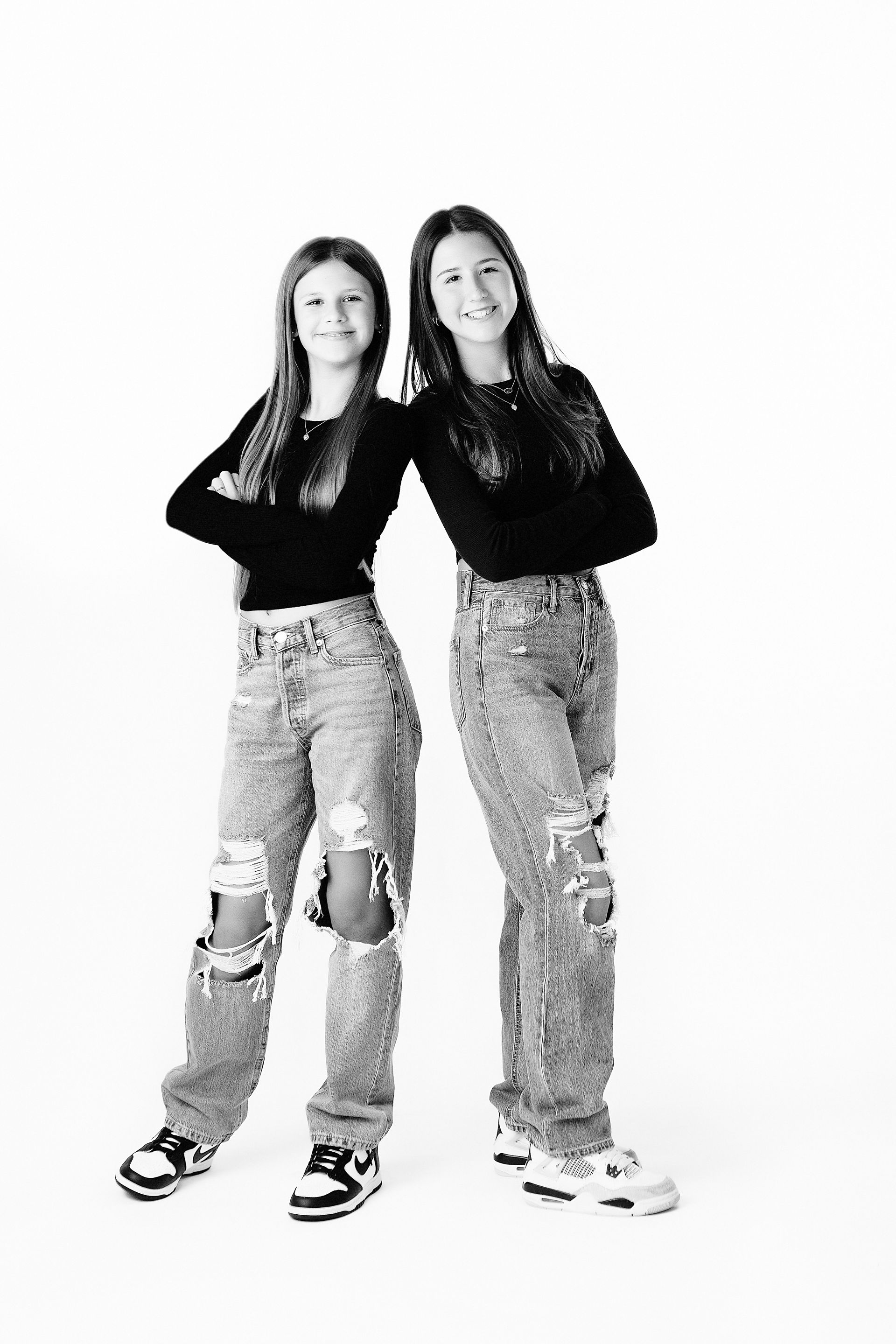 Two people in distressed jeans, black tops, arms crossed, standing. White background.