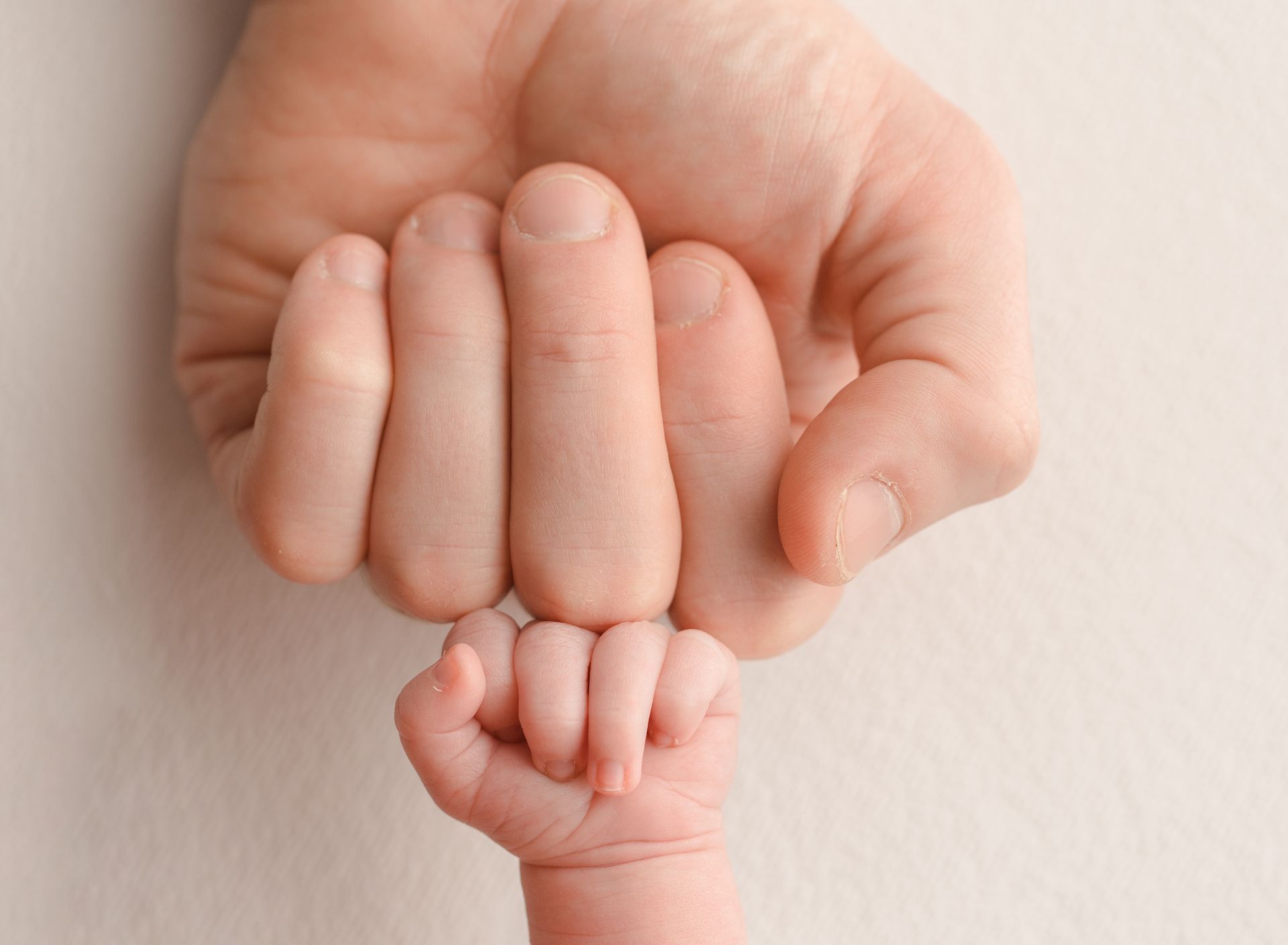 Adult hand gently holding a newborn's tiny fist.