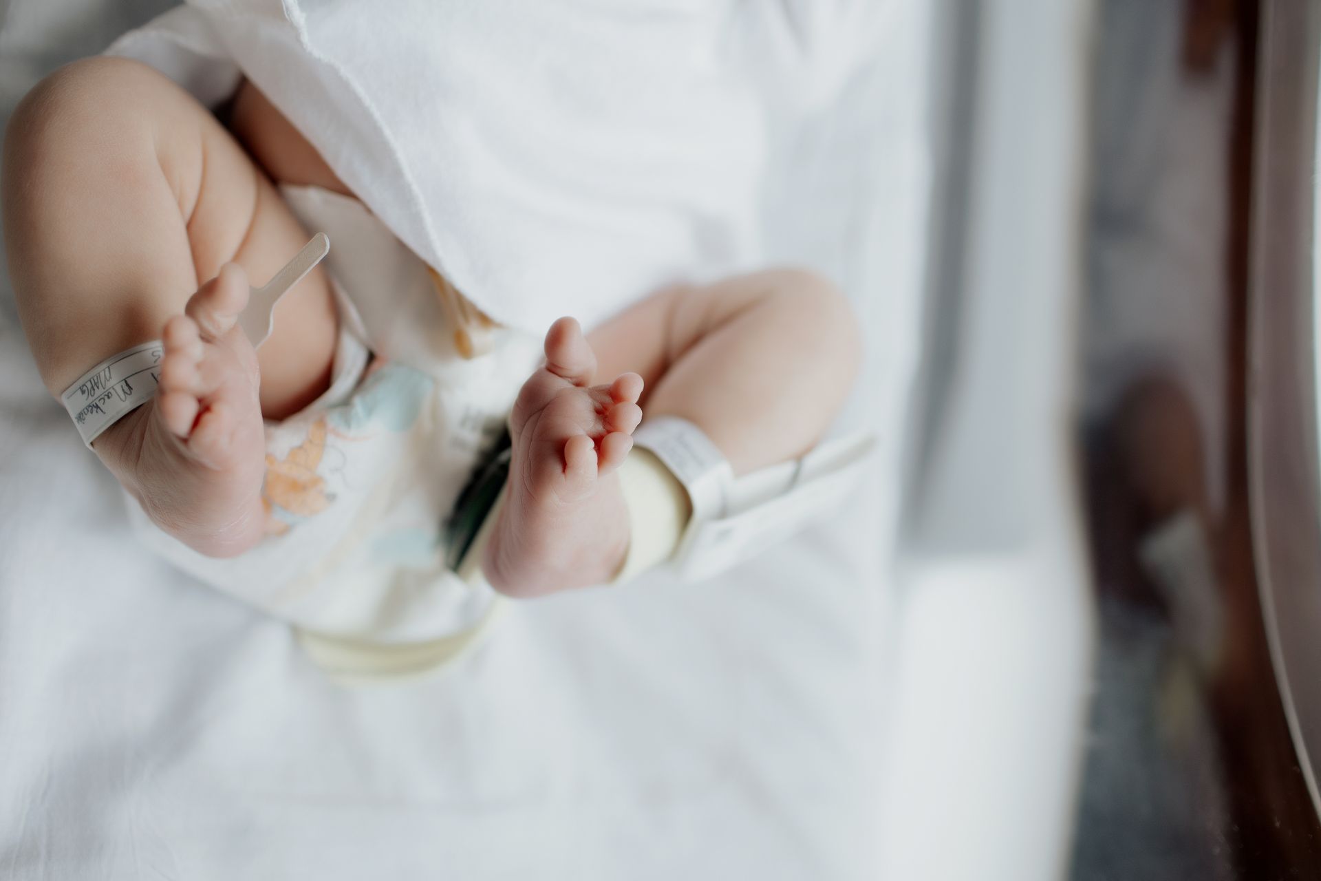 Newborn's feet with hospital ID tags, lying on a white sheet.