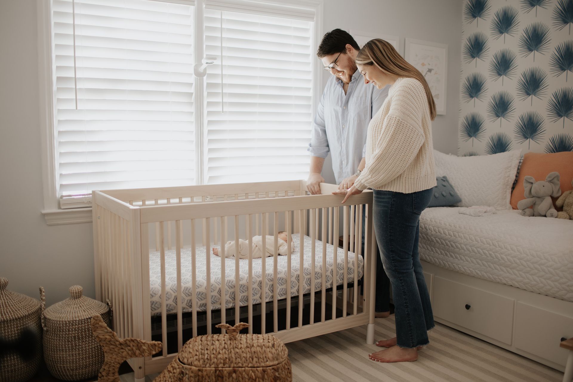 Parents are standing next to a crib in a nursery.