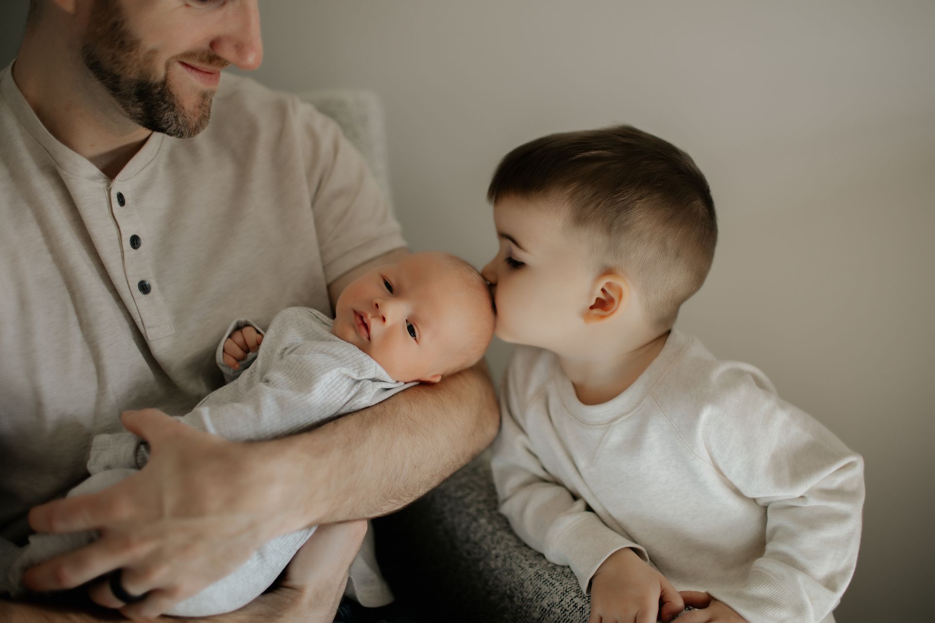 A man is holding a baby and a boy is kissing the baby on the head.