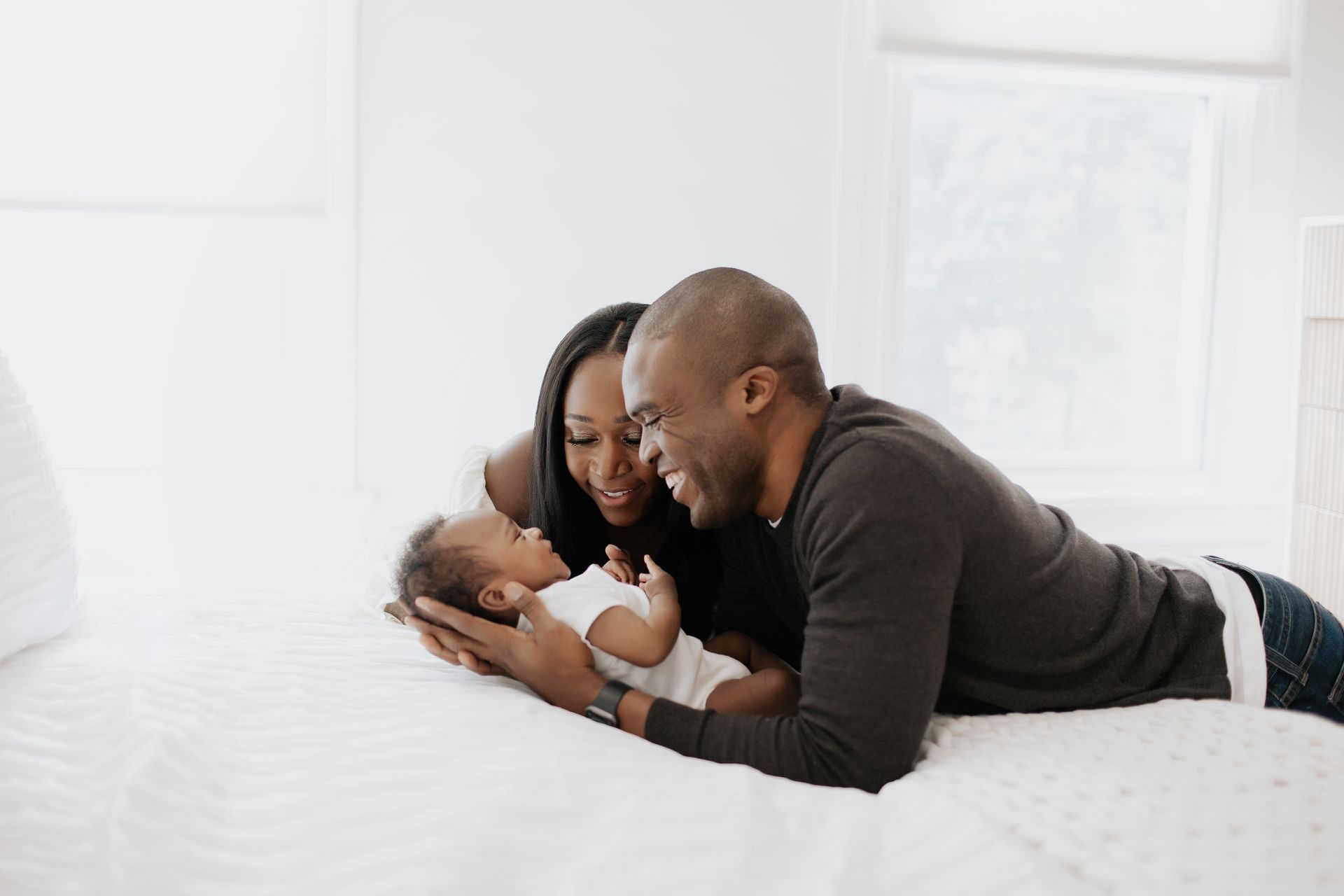 A man and woman are laying on a bed with a baby.