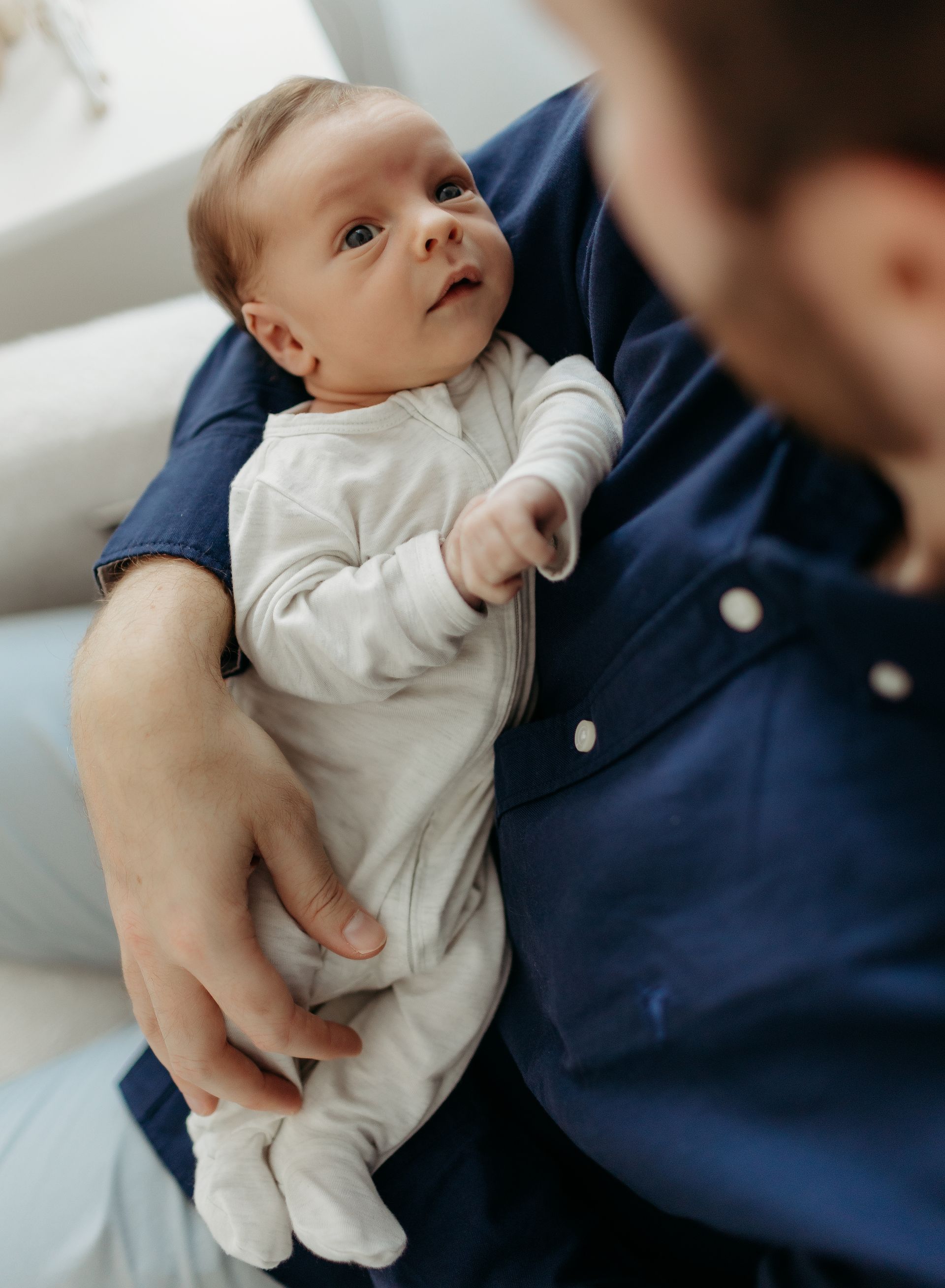 A man is holding a newborn baby in his arms as baby looks up at him.