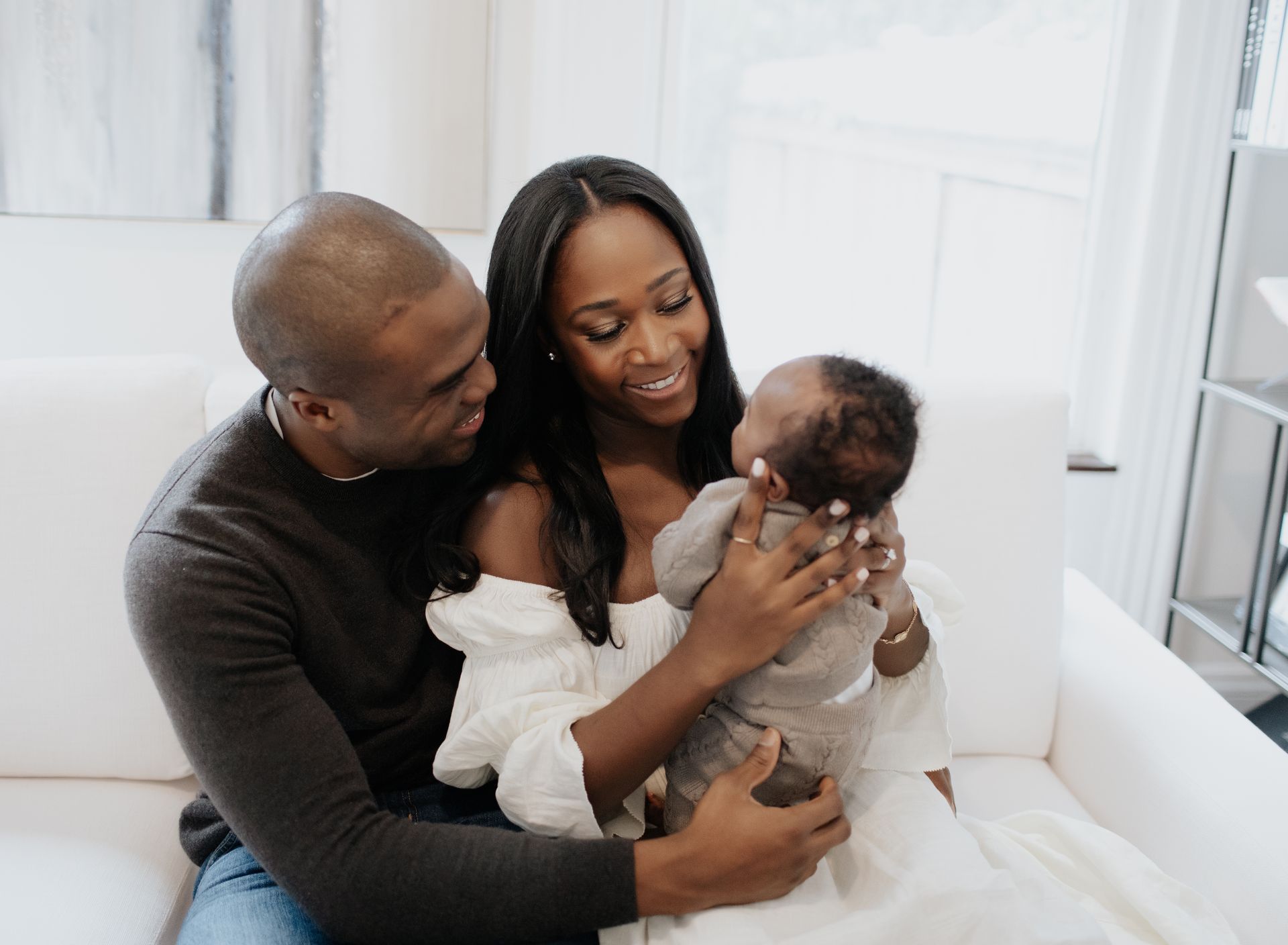 A man and woman are sitting on a couch holding a baby.