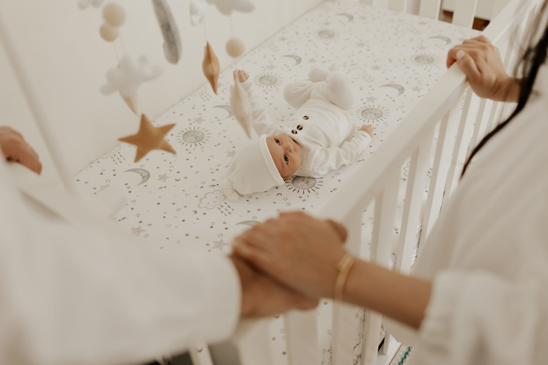 A woman and a man are holding hands by the crib overlooking baby.