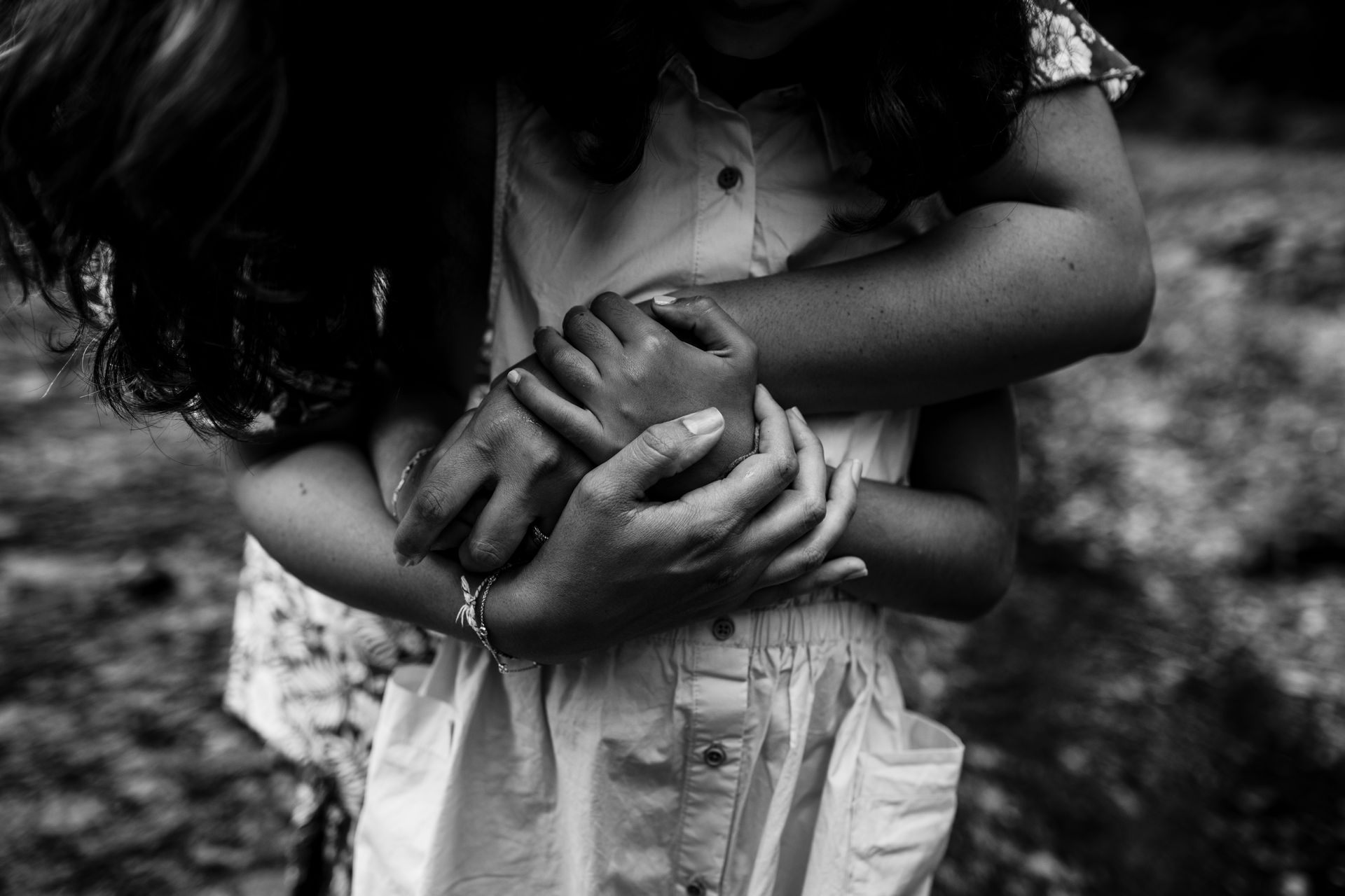 Person's arms wrapped around a child, hands clasped. Black and white.