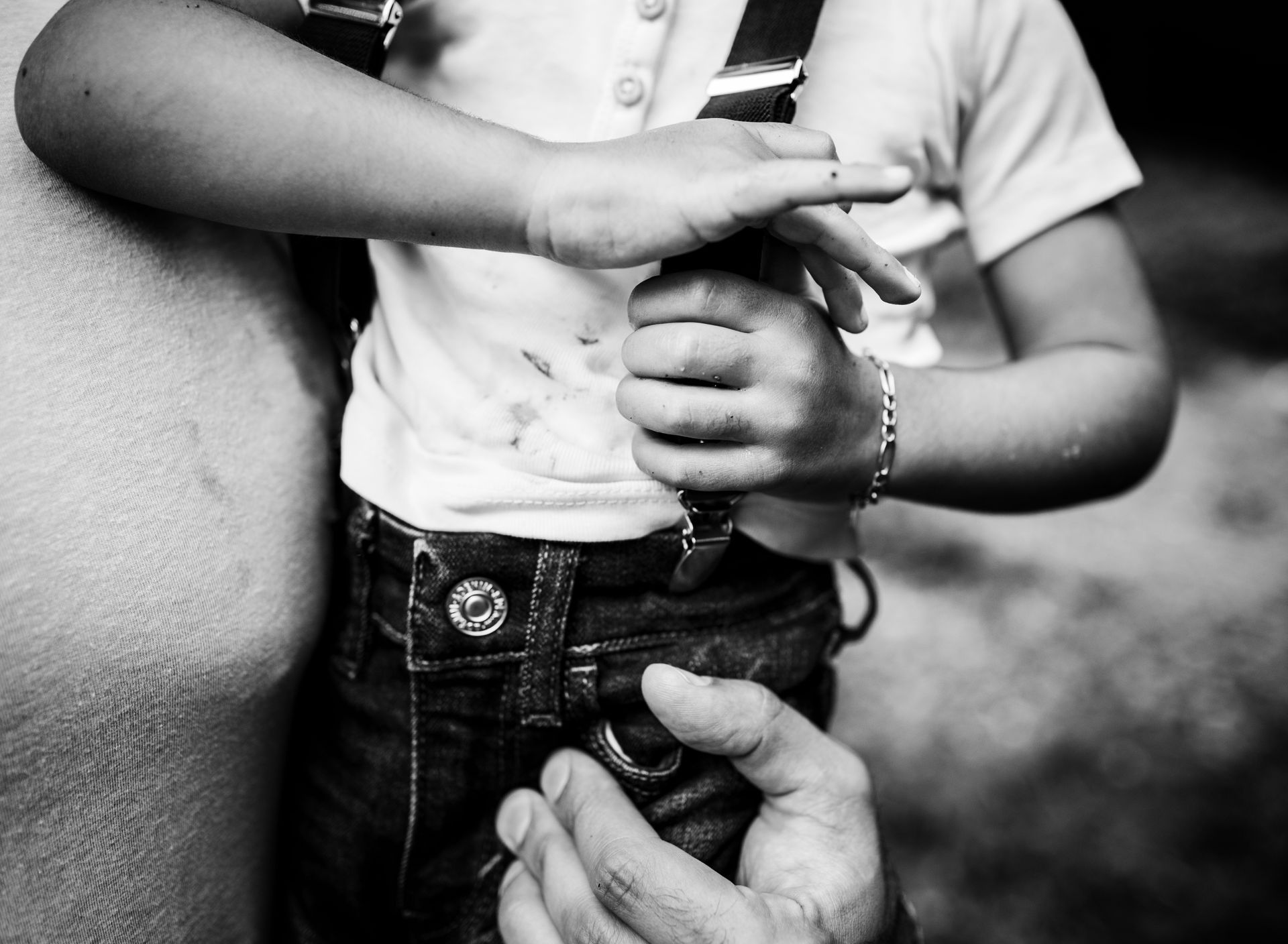 Child holding onto object, hand of adult below. Black and white.