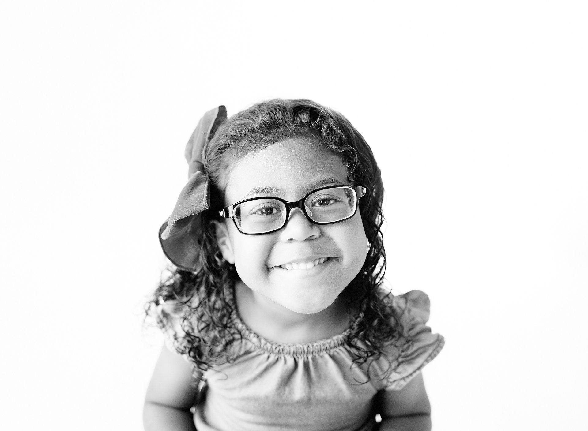 Smiling child wearing glasses and a large bow.