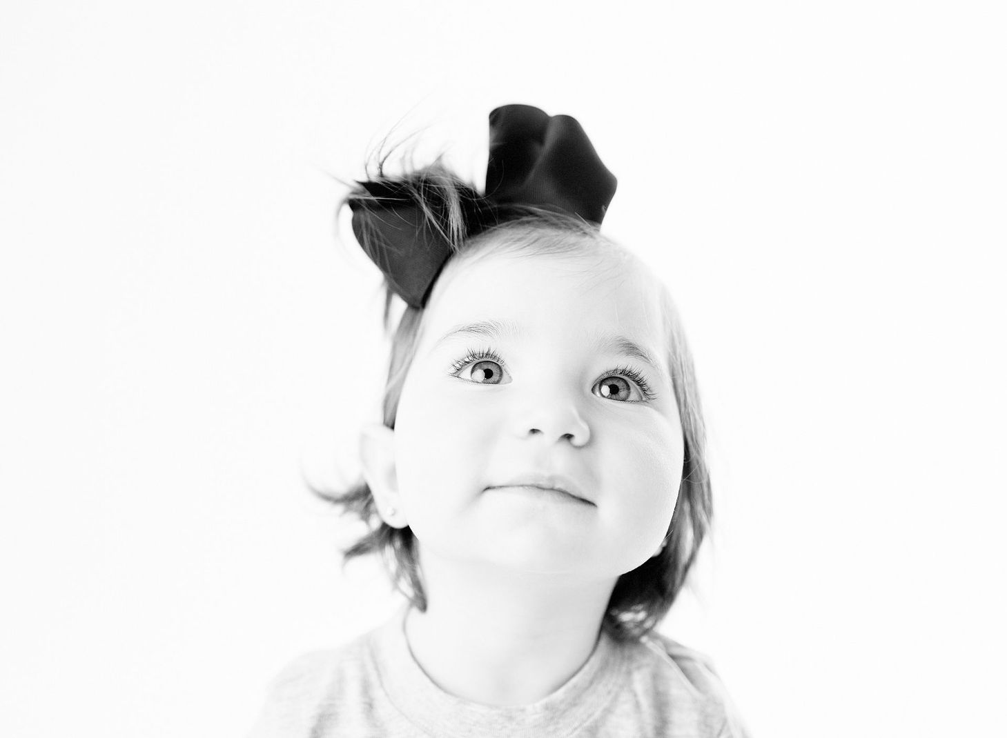 Child with a large black bow, looking upwards with a soft smile in Franklin Lakes, NJ.