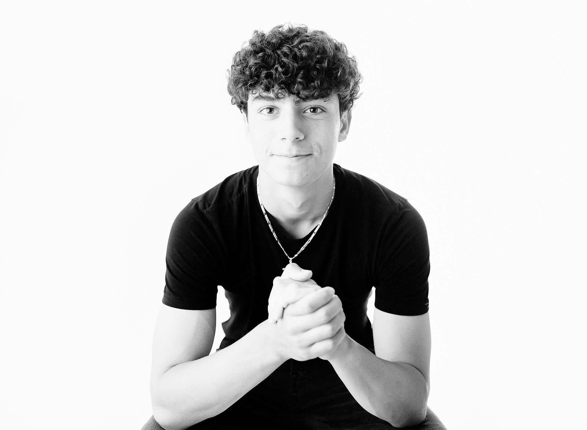 Young person with curly hair, in black shirt, clasped hands.