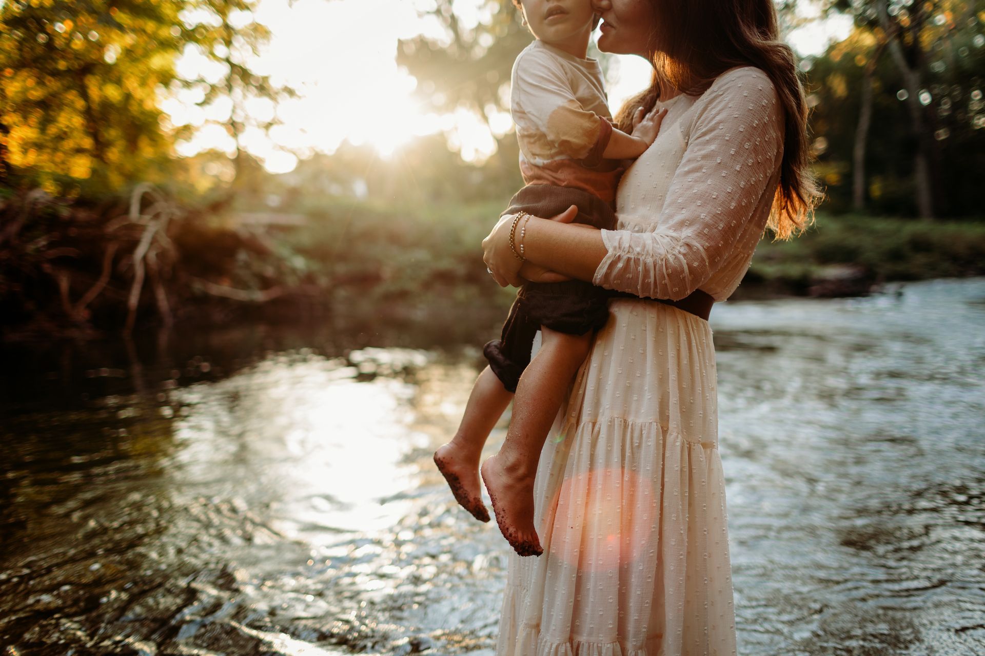 Woman holding child in a stream at sunset.
