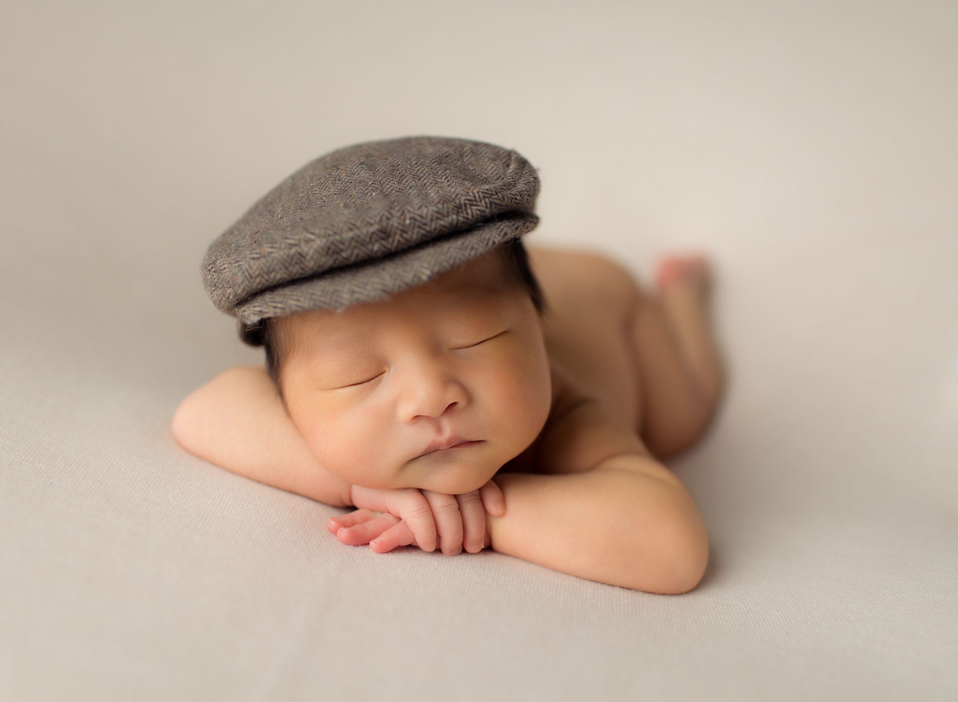 A newborn baby wearing a hat is sleeping on a blanket.