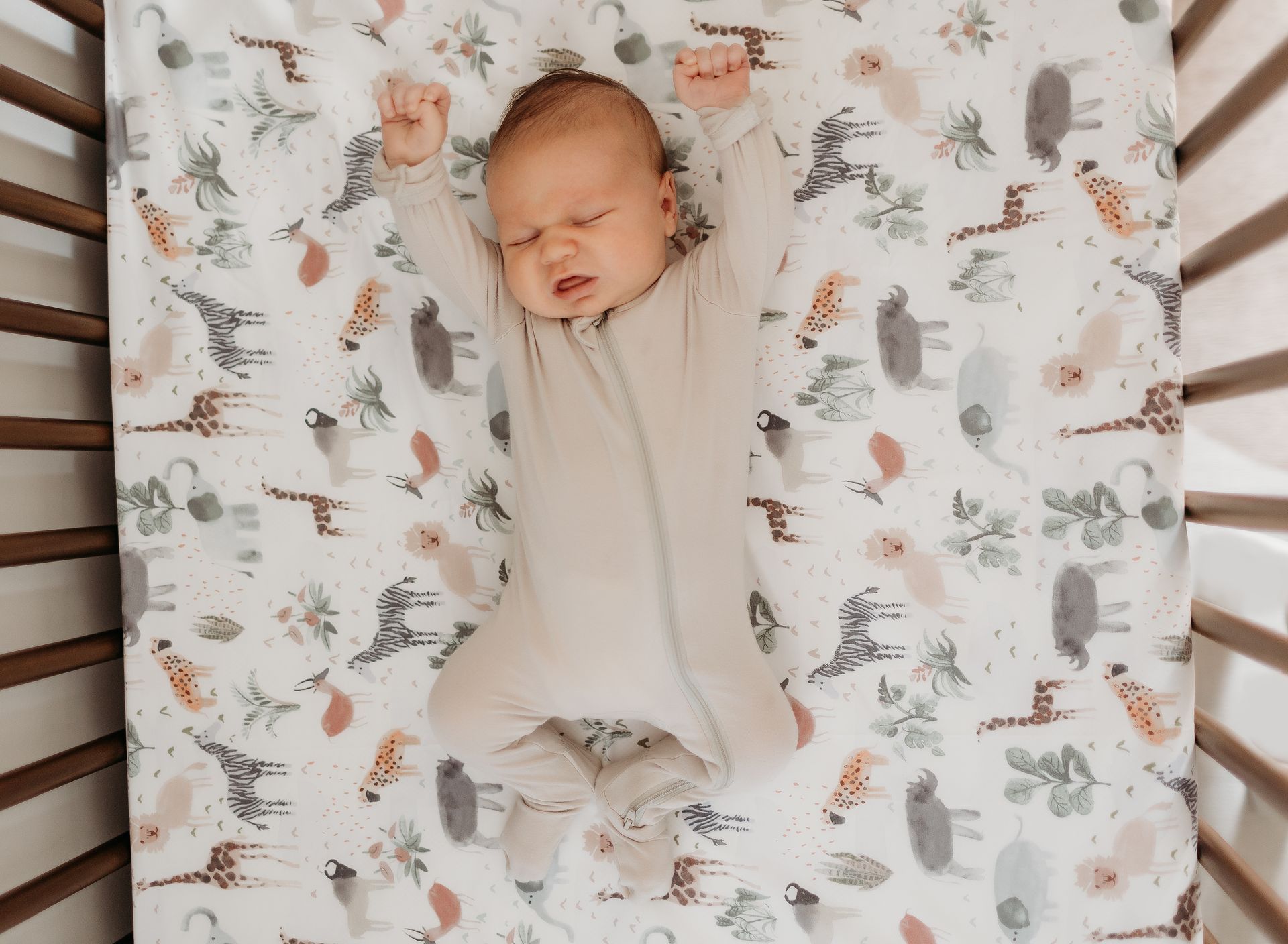 A baby is laying in a crib on a blanket with animals on it.